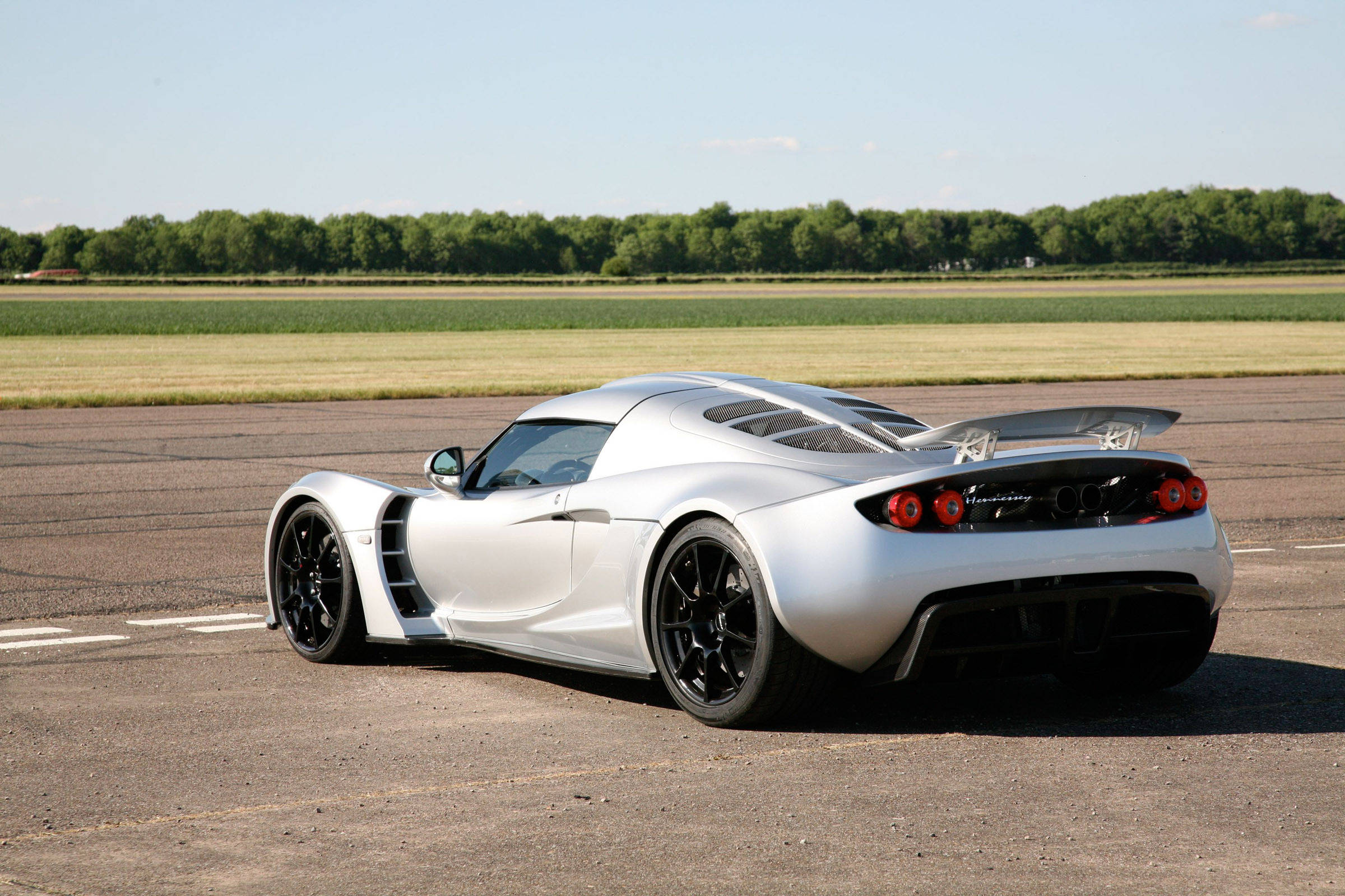 Hennessey Venom GT 壁紙 — 一架流線型銀色跑車配黑色輪胎，停泊在瀝青跑道上，天空湛藍。