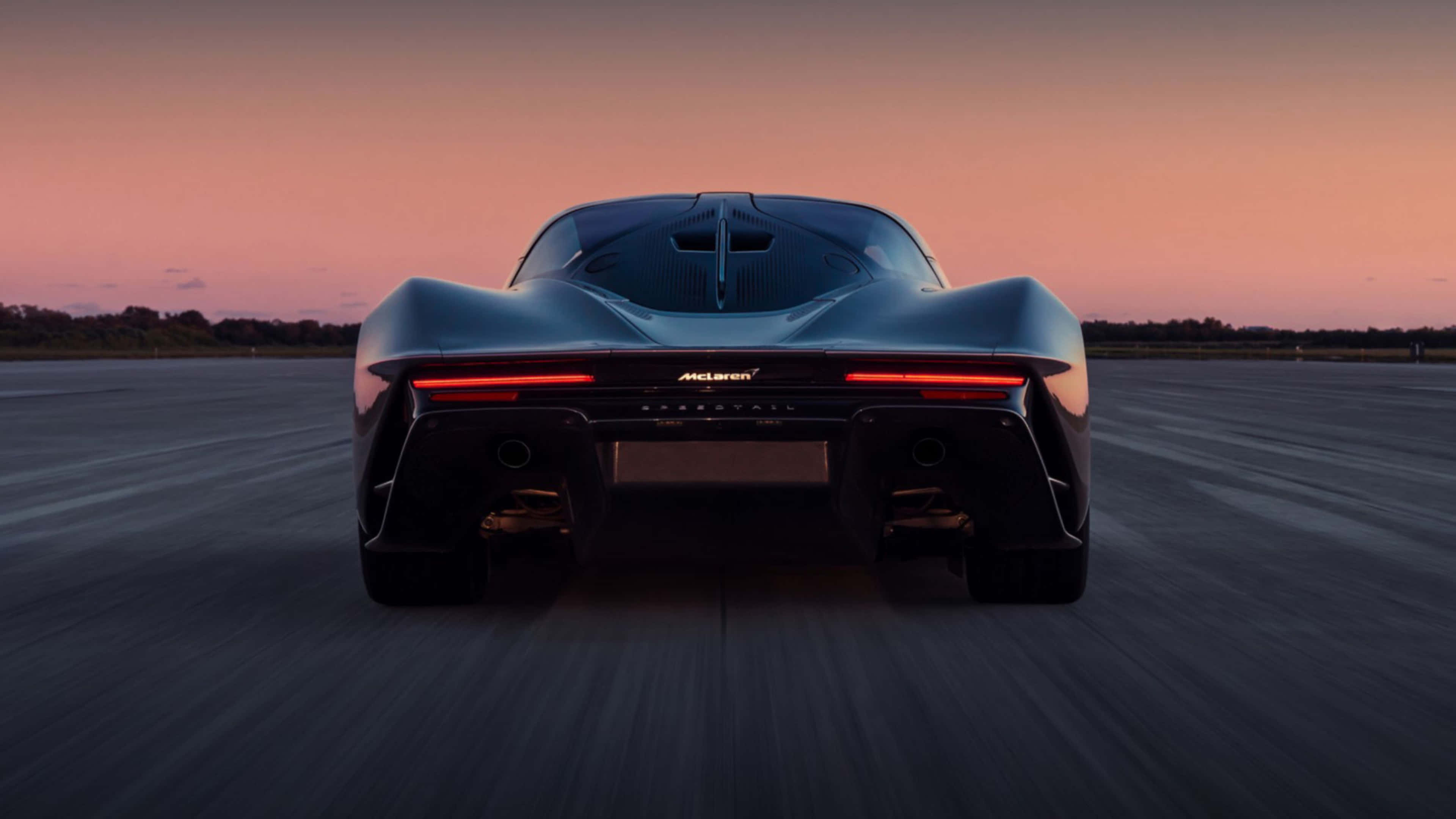 4K Car 桌布 壁紙 — 一架流線型麥拿侖超級跑車在日落時分的跑道上疾馳而去，紅色尾燈閃爍，天空呈現漸變色彩。