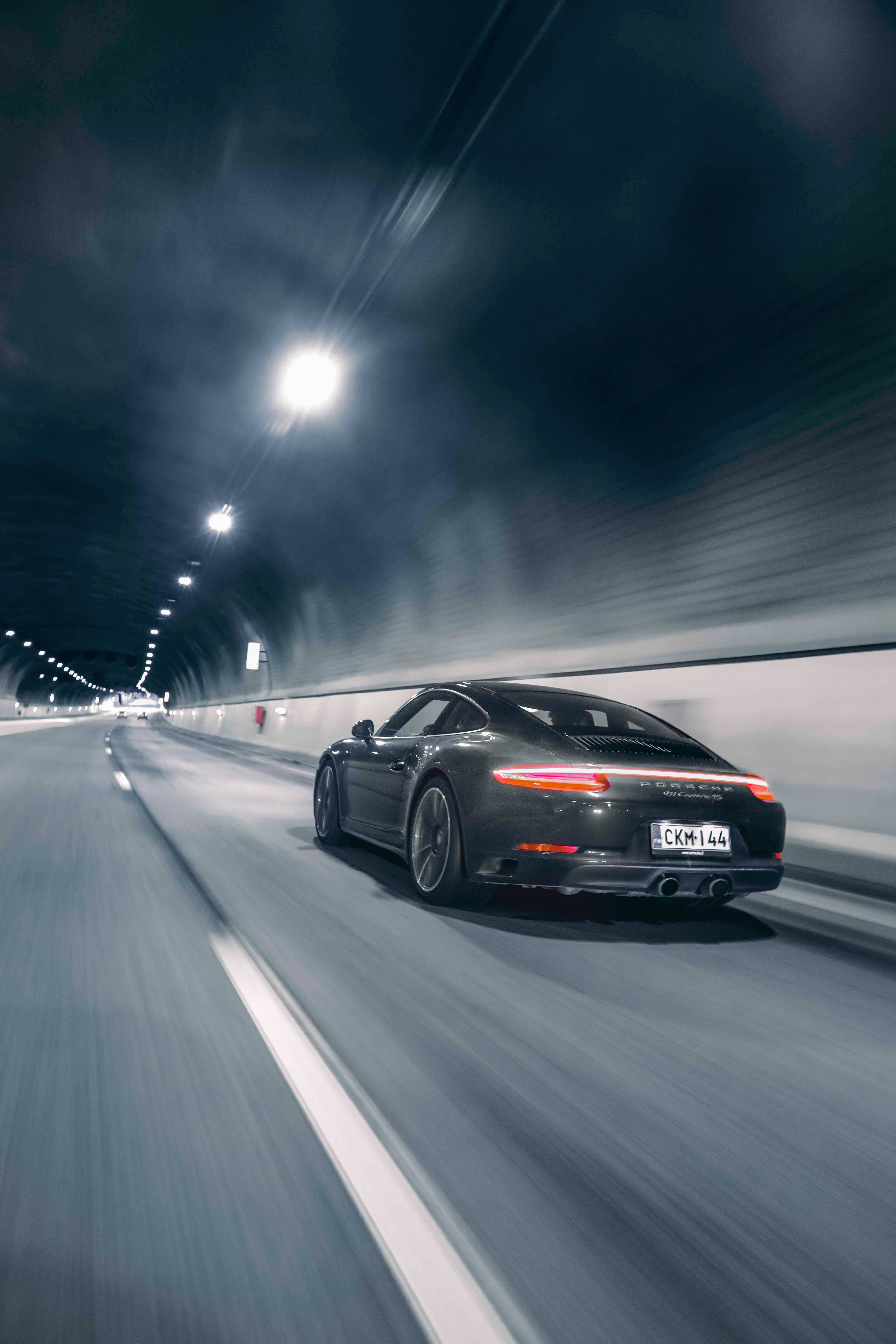 speeding car 桌布 壁紙 — 一架流線型黑色保時捷911在昏暗隧道中疾馳，動態模糊效果凸顯速度感。