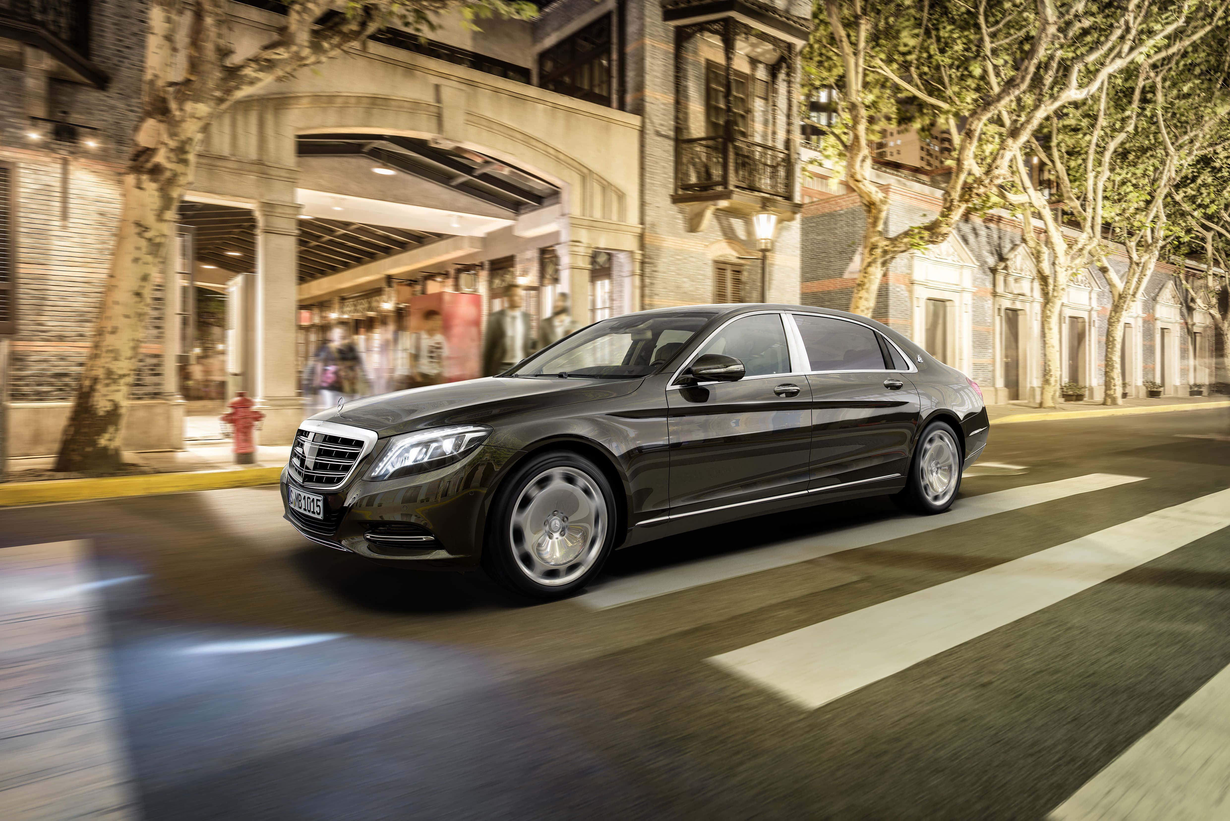 Maybach 桌布 壁紙 — 一架流線型黑色平治S-Class房車在夜間穿過溫暖燈光的歐洲城市街道，帶有模糊動感和發光的商店櫥窗。