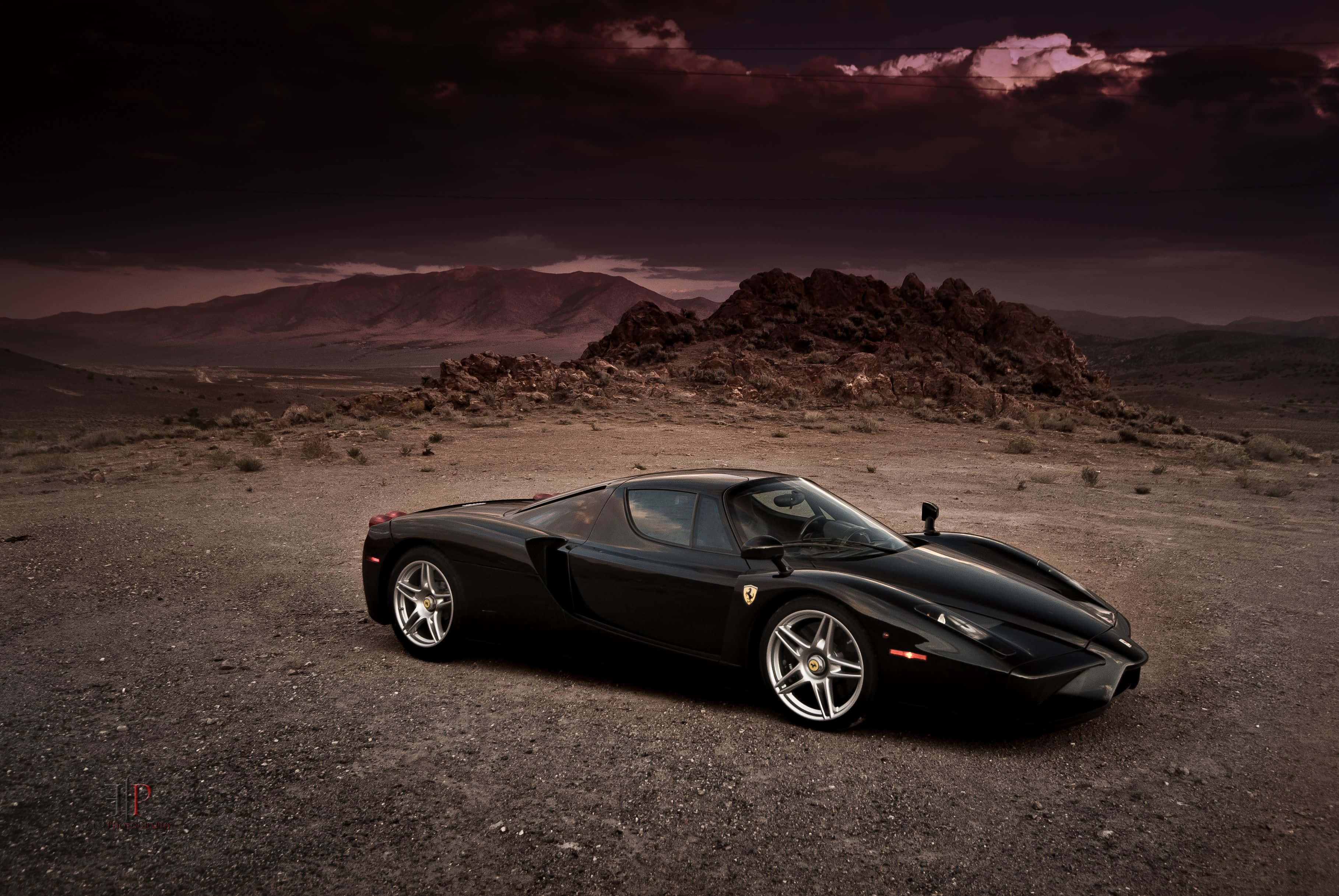 Ferrari Enzo 桌布 壁紙 — 一架流線型黑色法拉利Enzo停泊在荒蕪的沙漠景觀中，天空佈滿戲劇性的紫色和深色雲層。