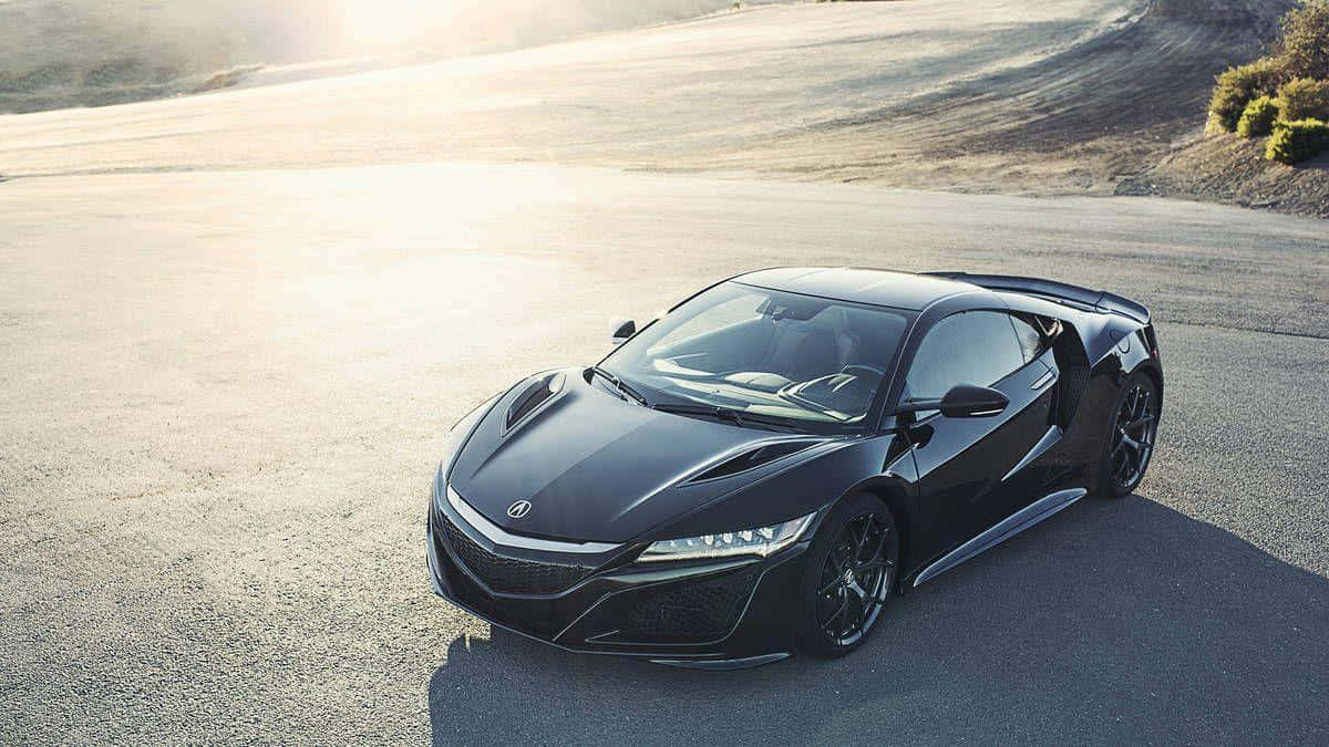 Acura Nsx 桌布 壁紙 — 一架流線型黑色跑車在金色陽光下閃耀，行駛在蜿蜒的瀝青路上，周圍是乾燥的山丘。