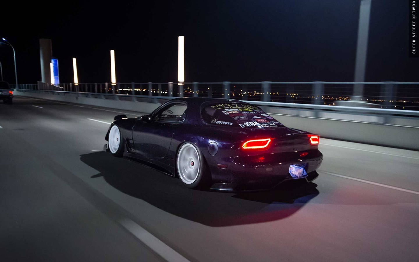 Mazda 桌布 壁紙 — 一架深紫色改裝跑車在夜間行駛於燈火通明的橋上，遠處城市燈光閃爍。