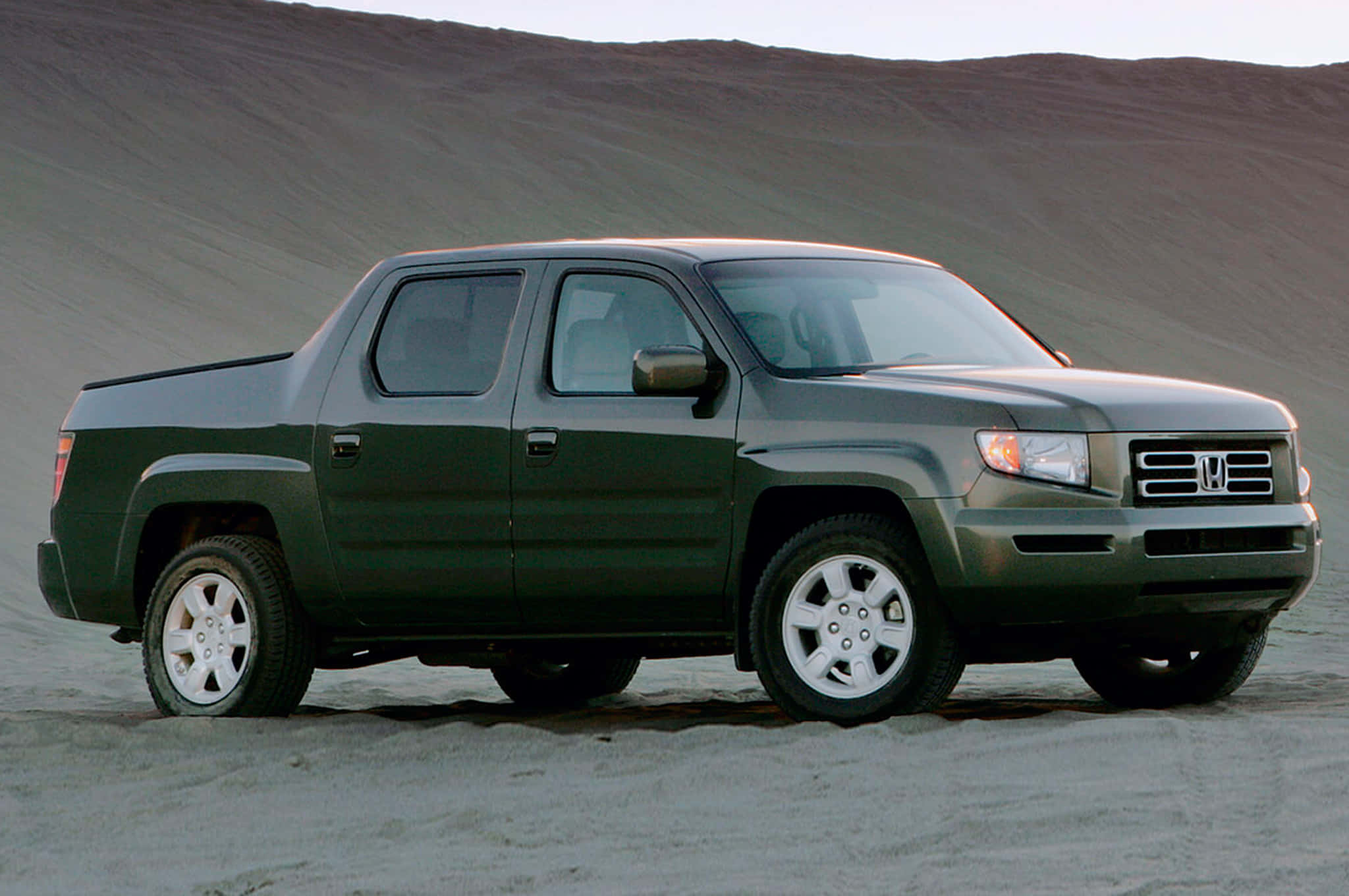 Honda Ridgeline 桌布 壁紙 — 一架深綠色本田Ridgeline皮卡車停在沙地上，背景有起伏的山丘。