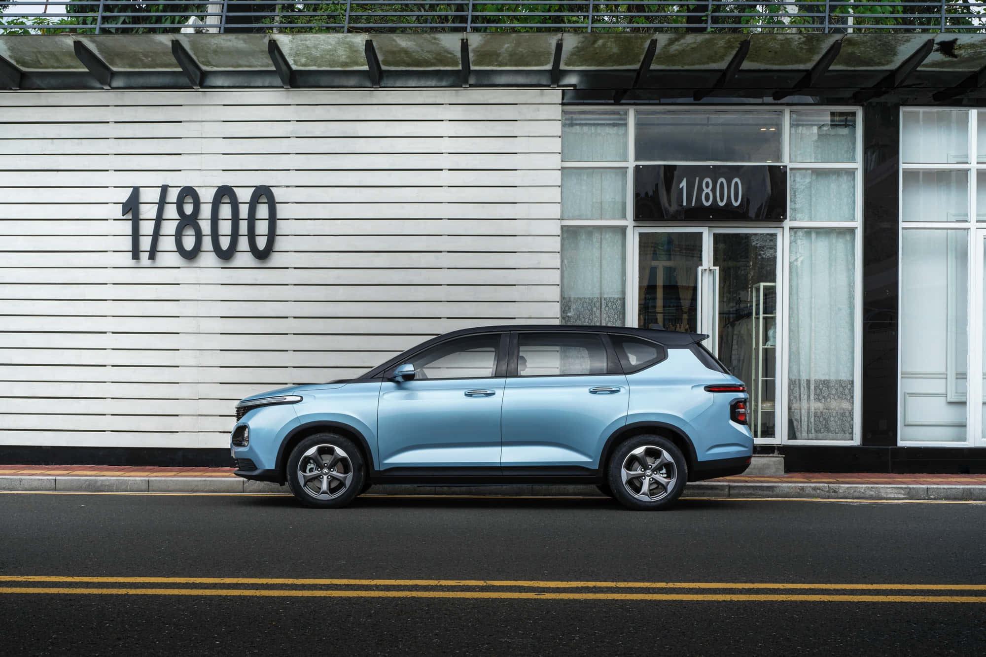Baojun 桌布 壁紙 — 一架淺藍色SUV停泊喺一條街旁邊，隔籬係一棟現代建築，白色板條牆上有「1/800」標誌。