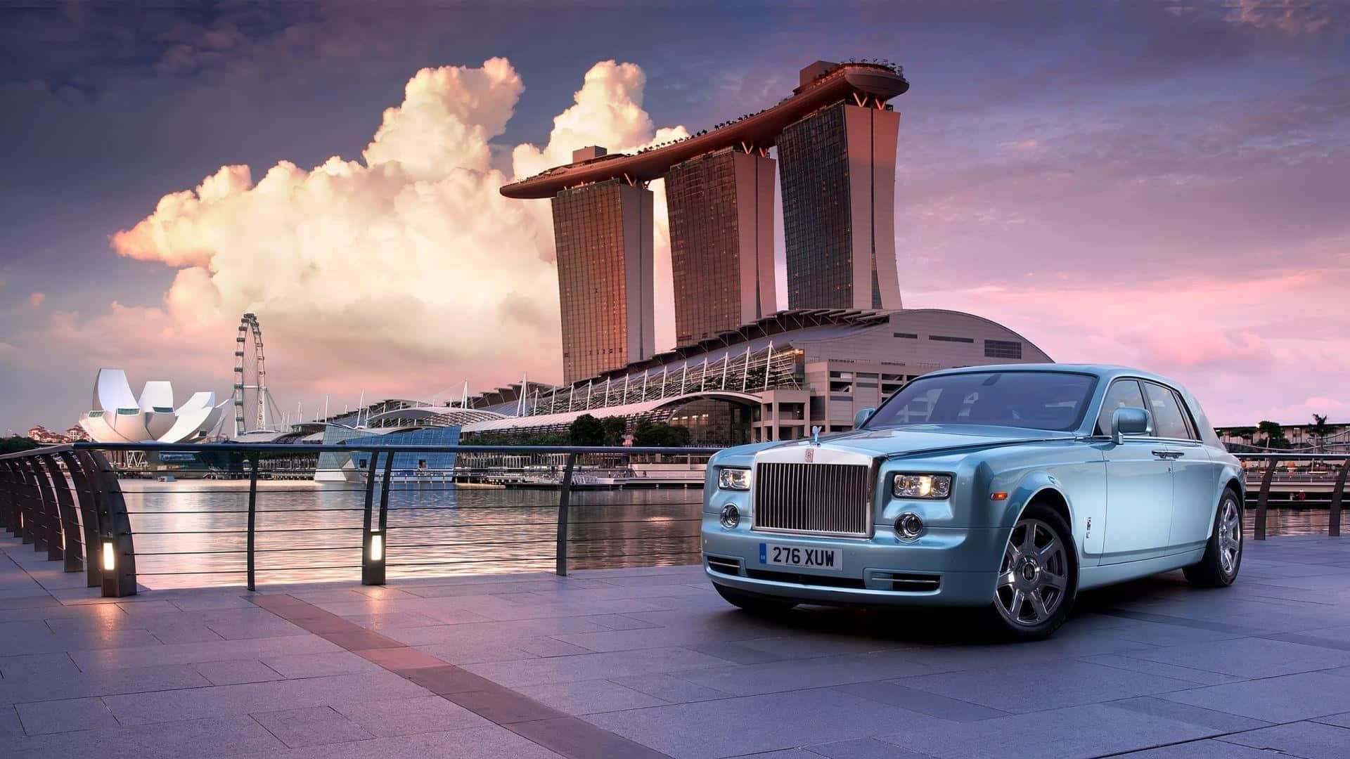 Rolls Royce 桌布 壁紙 — 一架淺藍色勞斯萊斯幻影停泊在海濱長廊，濱海灣金沙和新加坡天際線在日落時閃耀。