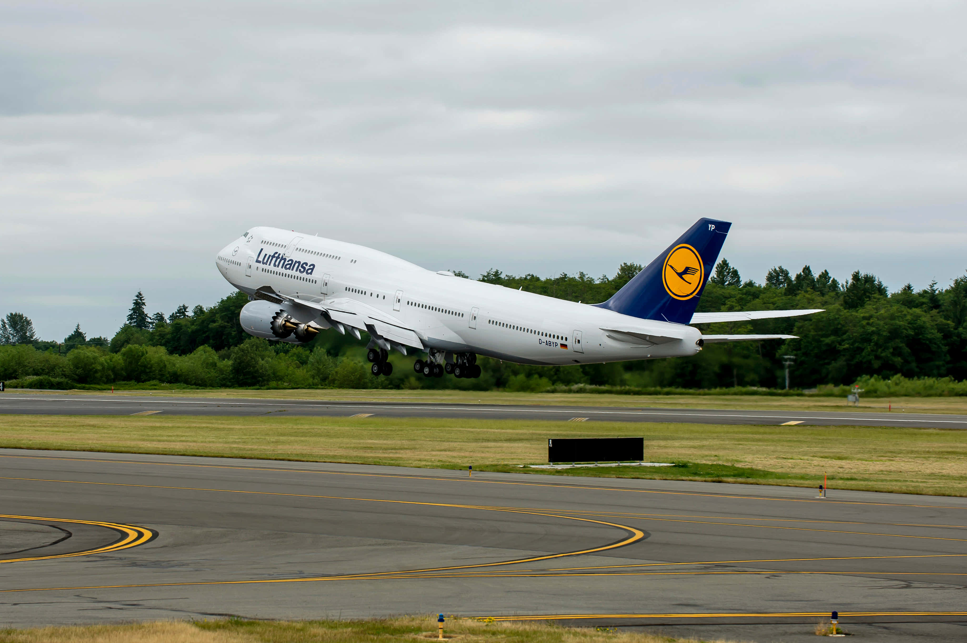 Jumbo Jets 桌布 壁紙 — 一架漢莎航空波音747從跑道起飛，背景有樹木和陰天。