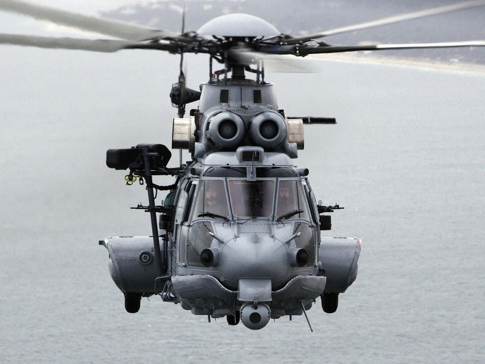Helicopter 桌布 壁紙 — 一架灰色軍用直升機低空盤旋在平靜的海面上，旋翼槳葉因運動而模糊。