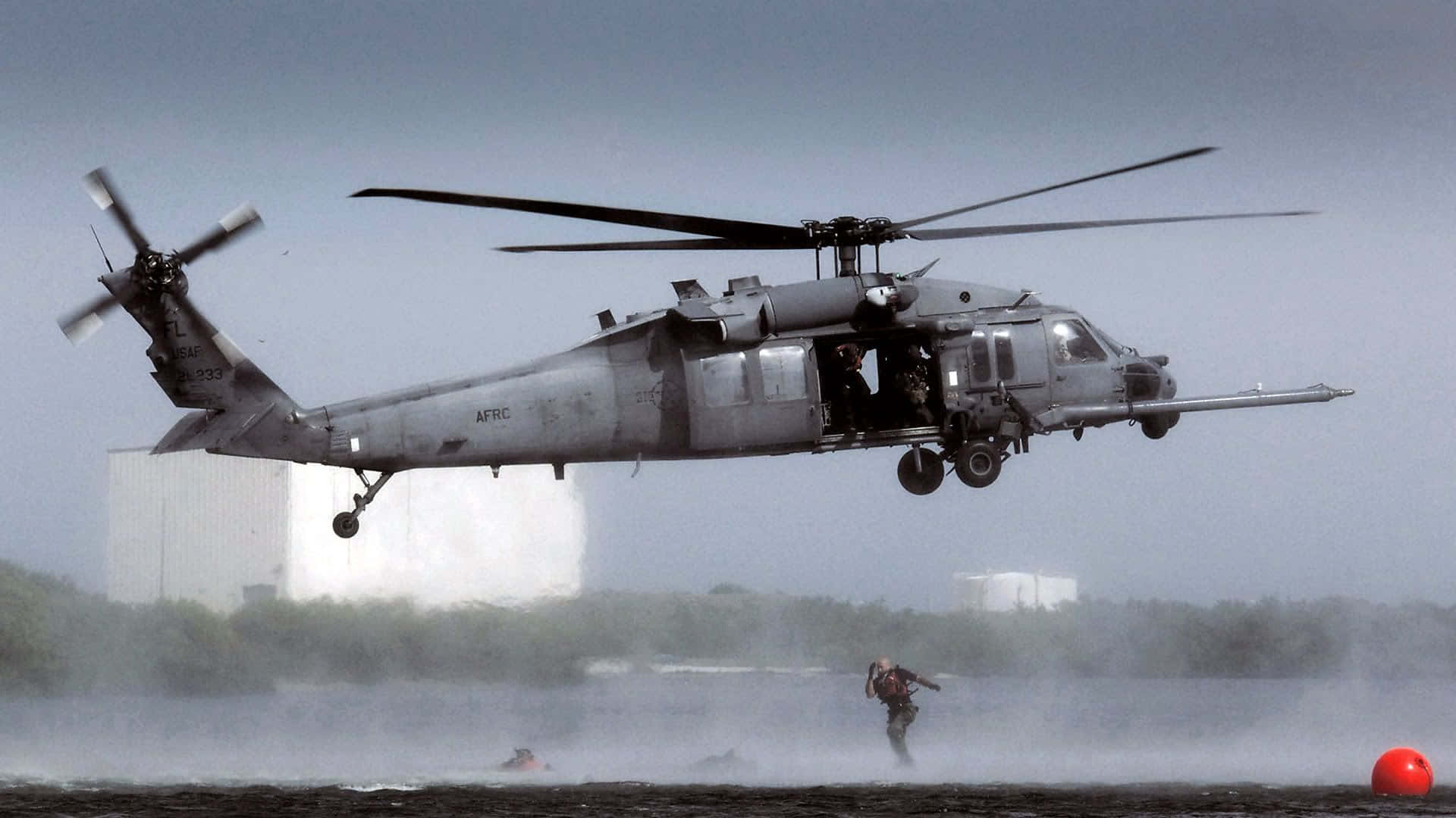 Helicopter 桌布 壁紙 — 一架灰色軍用直升機低空盤旋在水面上，附近有一個人正在游泳，並可見一個紅色浮標。
