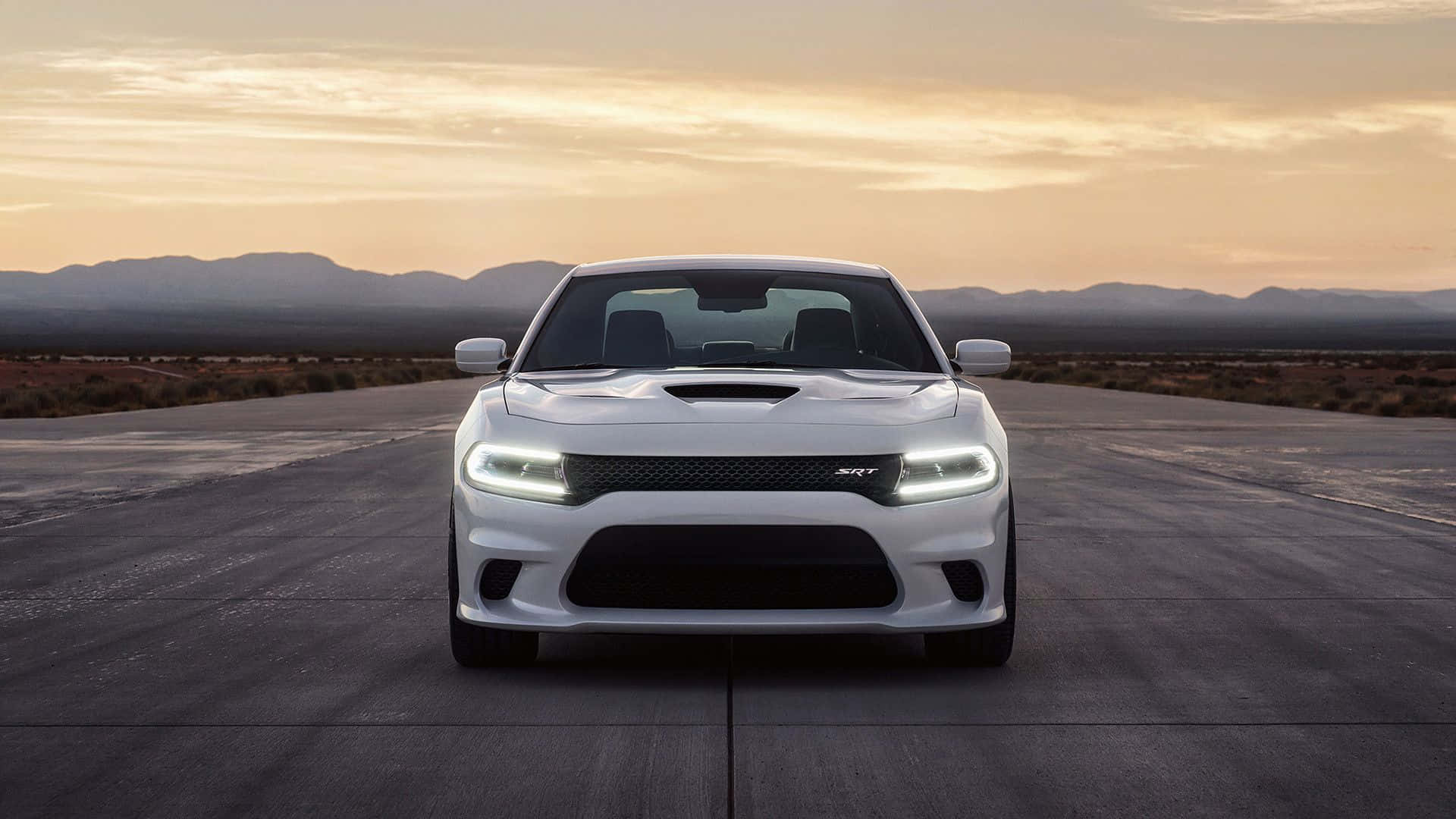 Dodge Charger 桌布 壁紙 — 一架白色 Dodge Challenger SRT 在沙漠公路上向前行駛，背景是日落和山脈。