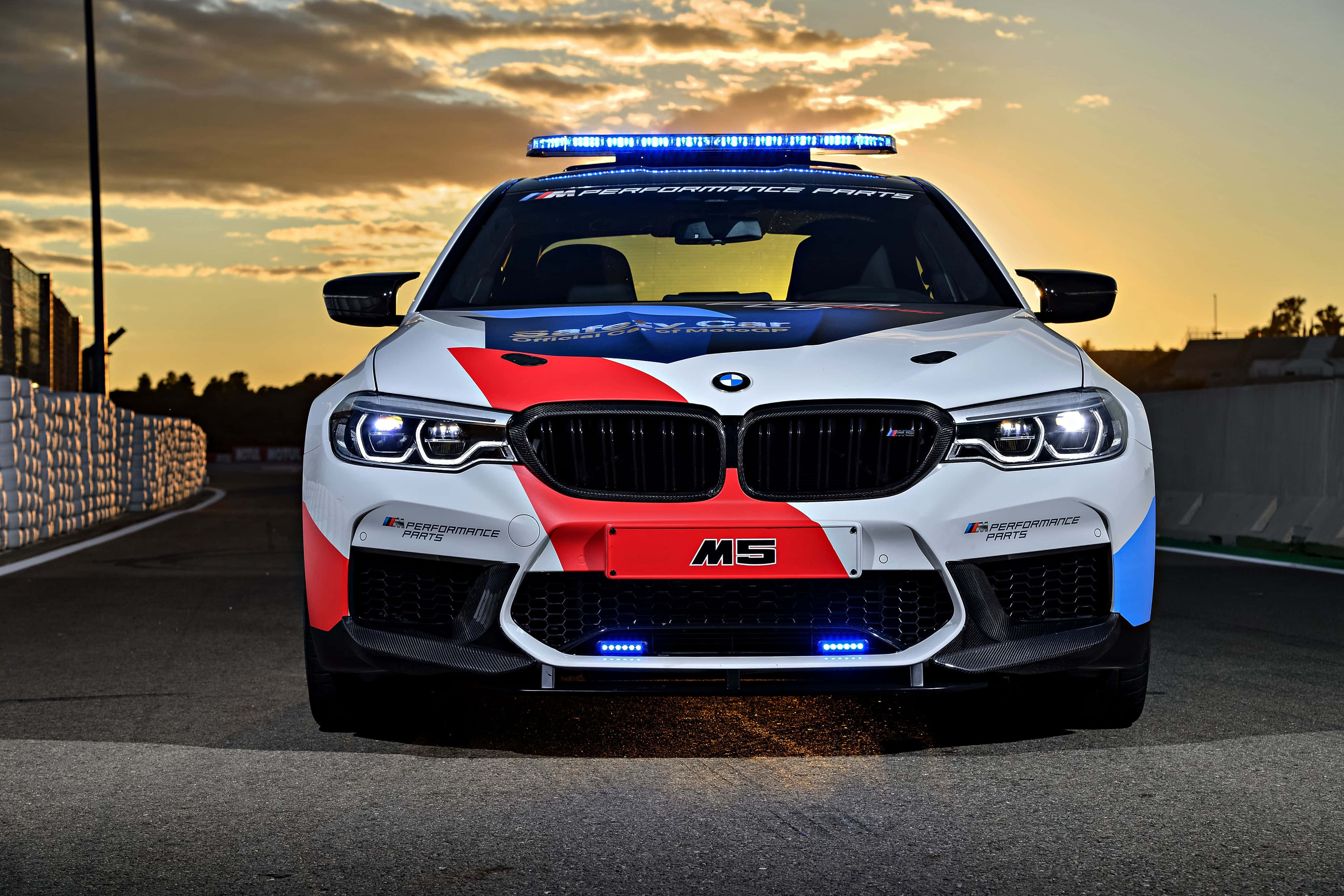 賽道上的安全車 壁紙 — 一架白色、紅色和藍色的BMW M5賽車，在日落時分的賽道上亮著閃燈向前行駛。