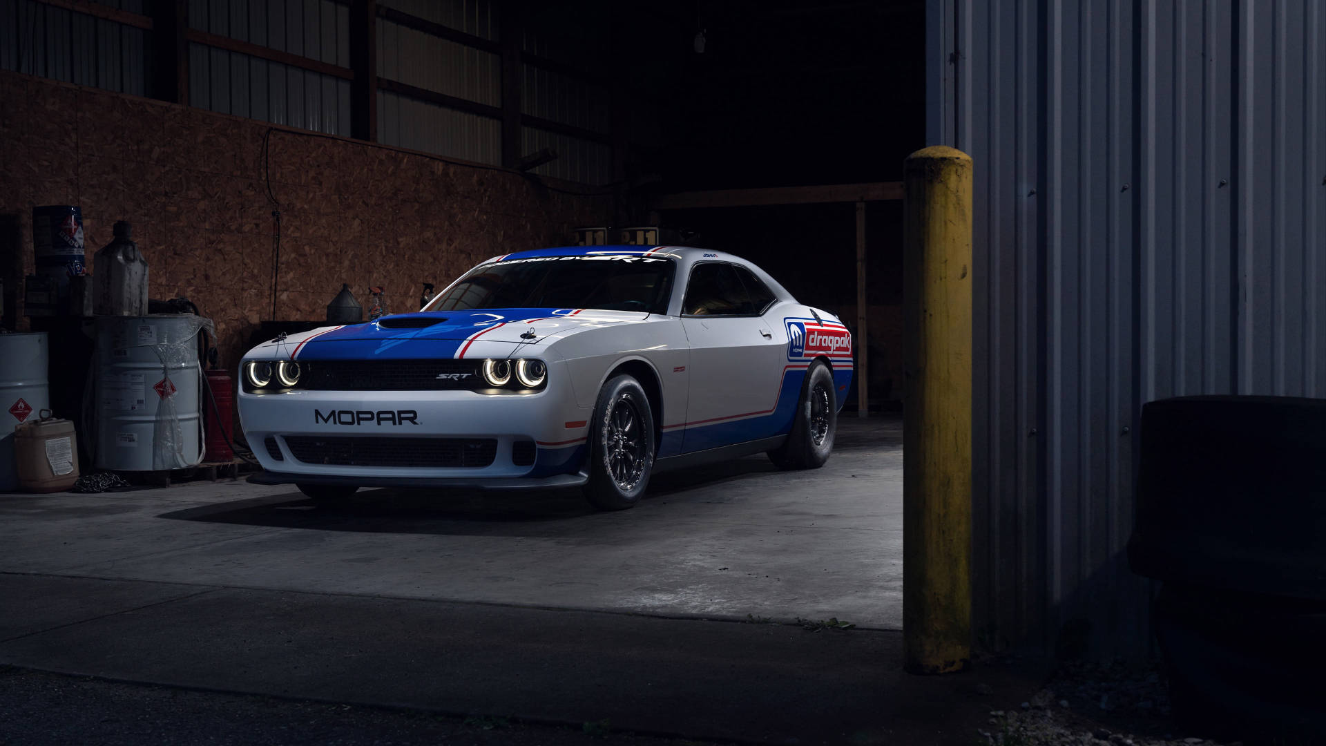 Sports Car 桌布 壁紙 — 一架白色、藍色和紅色的Mopar Dodge Challenger賽車停放在光線昏暗的車庫中，旁邊有工業用桶和黃色柱子。