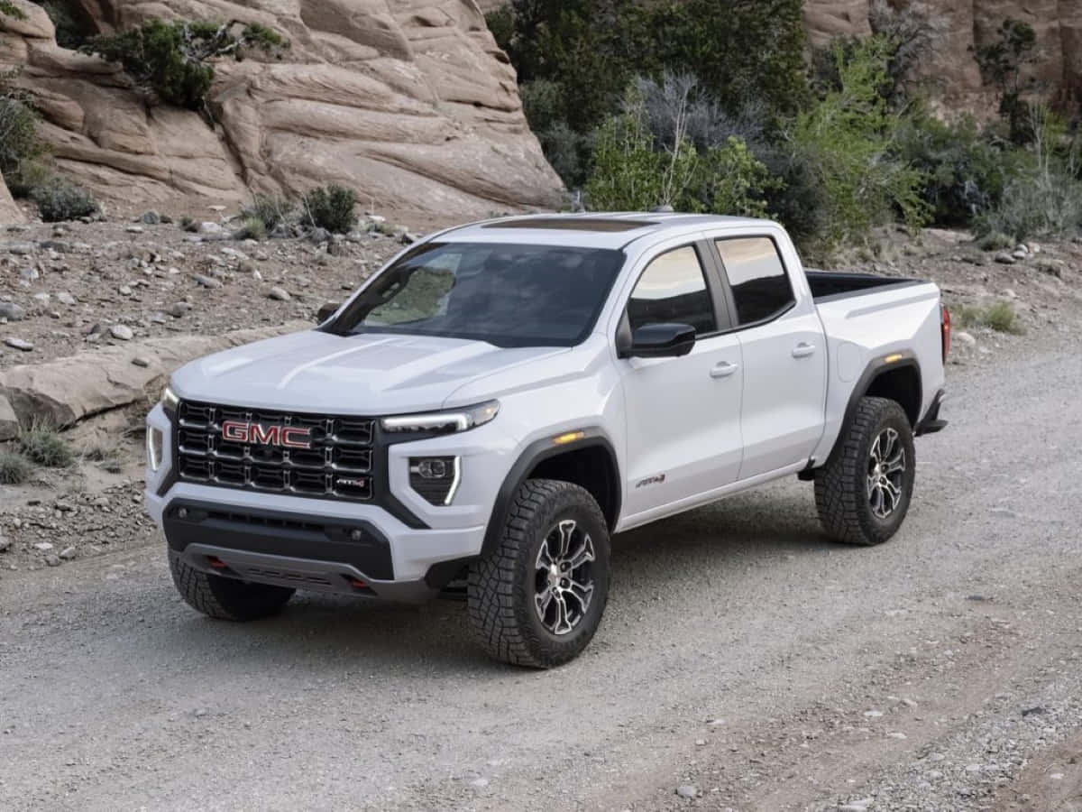 Gmc Canyon 桌布 壁紙 — 一架白色GMC Canyon AT4皮卡車停泊在碎石路上，旁邊是岩石沙漠地形，植被稀疏。
