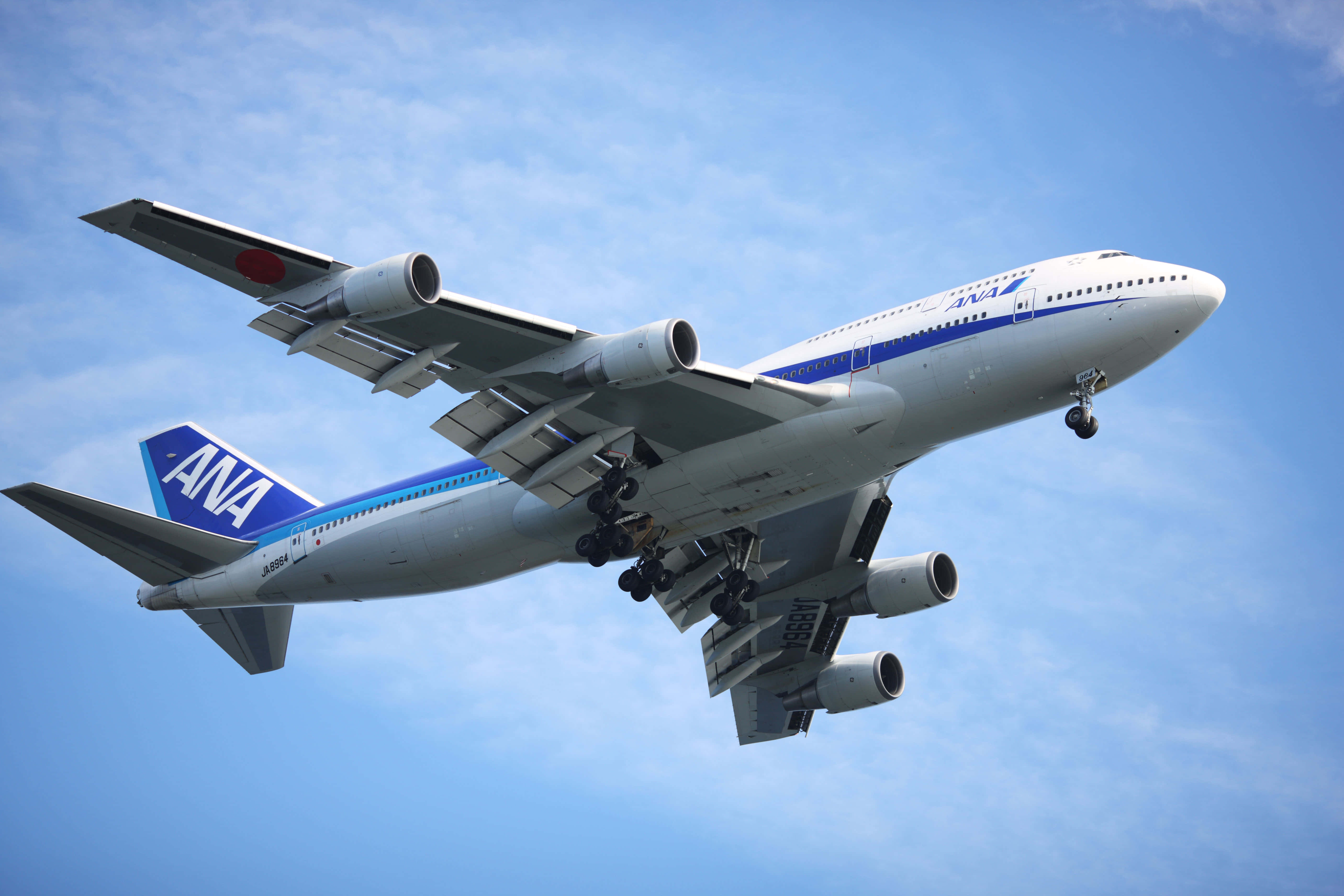 Jumbo Jets 桌布 壁紙 — 一架白色和藍色的ANA波音747飛機放下起落架，在晴朗的藍天中翱翔，伴隨著縷縷白雲。