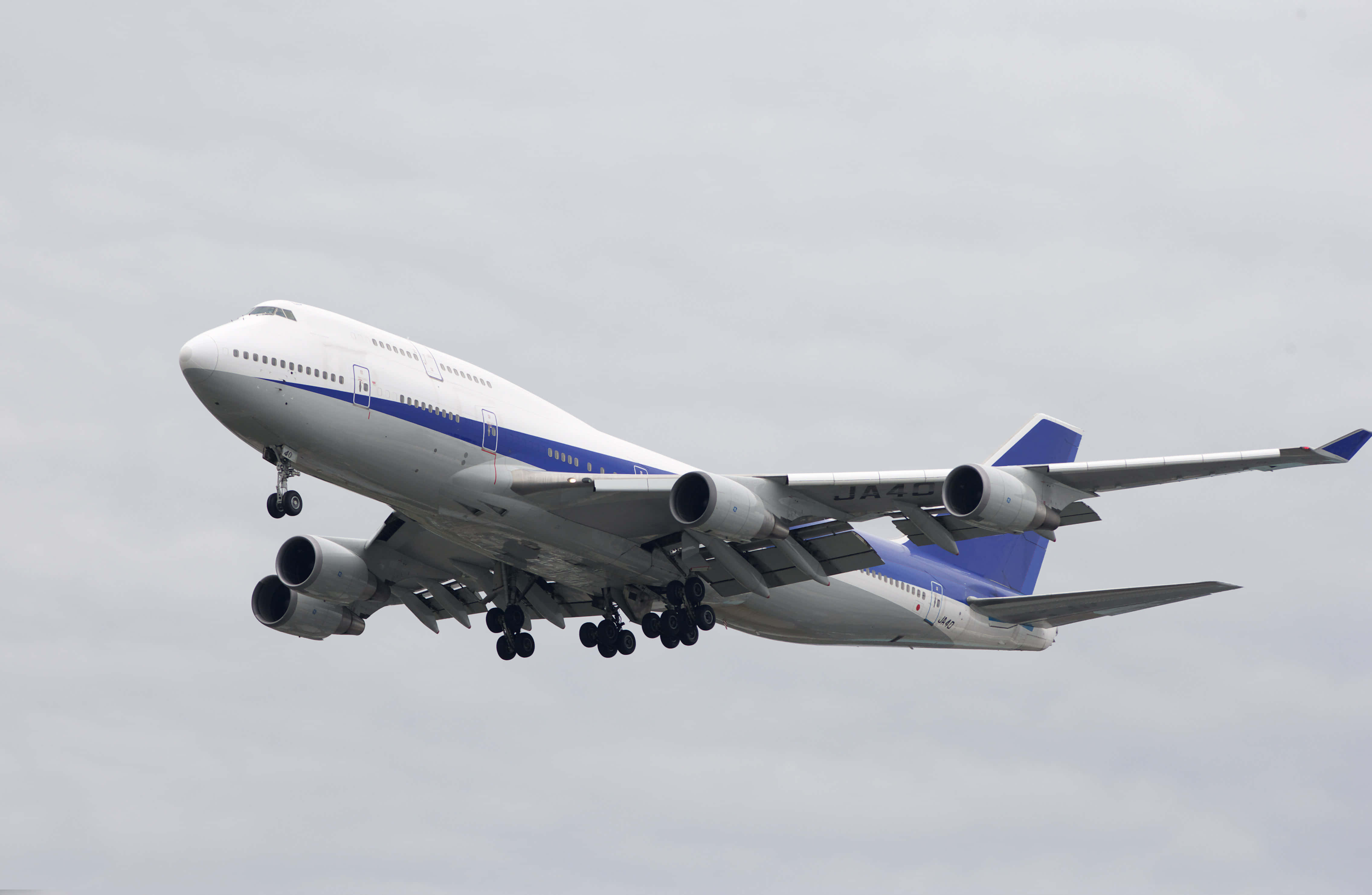 Jumbo Jets 桌布 壁紙 — 一架白色和藍色的波音747飛機放下起落架，在陰雲密佈的灰色天空中飛行。