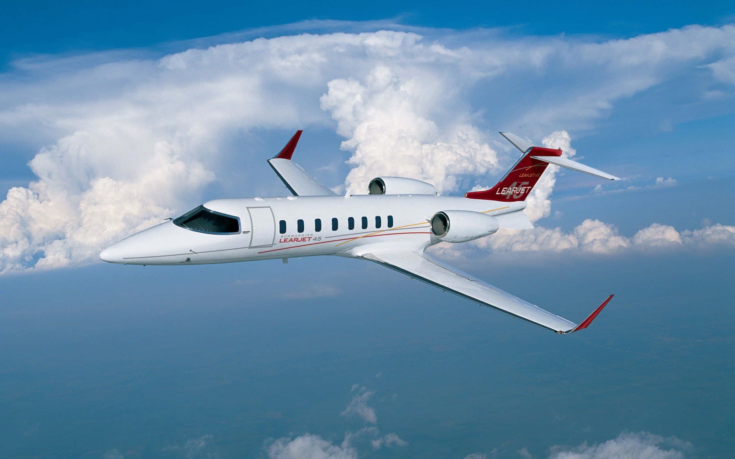 Jet 桌布 壁紙 — 一架白色嘅 Learjet 60 私人飛機喺鮮藍色天空背景下，優雅咁翱翔喺 fluffy 白色雲層之上。