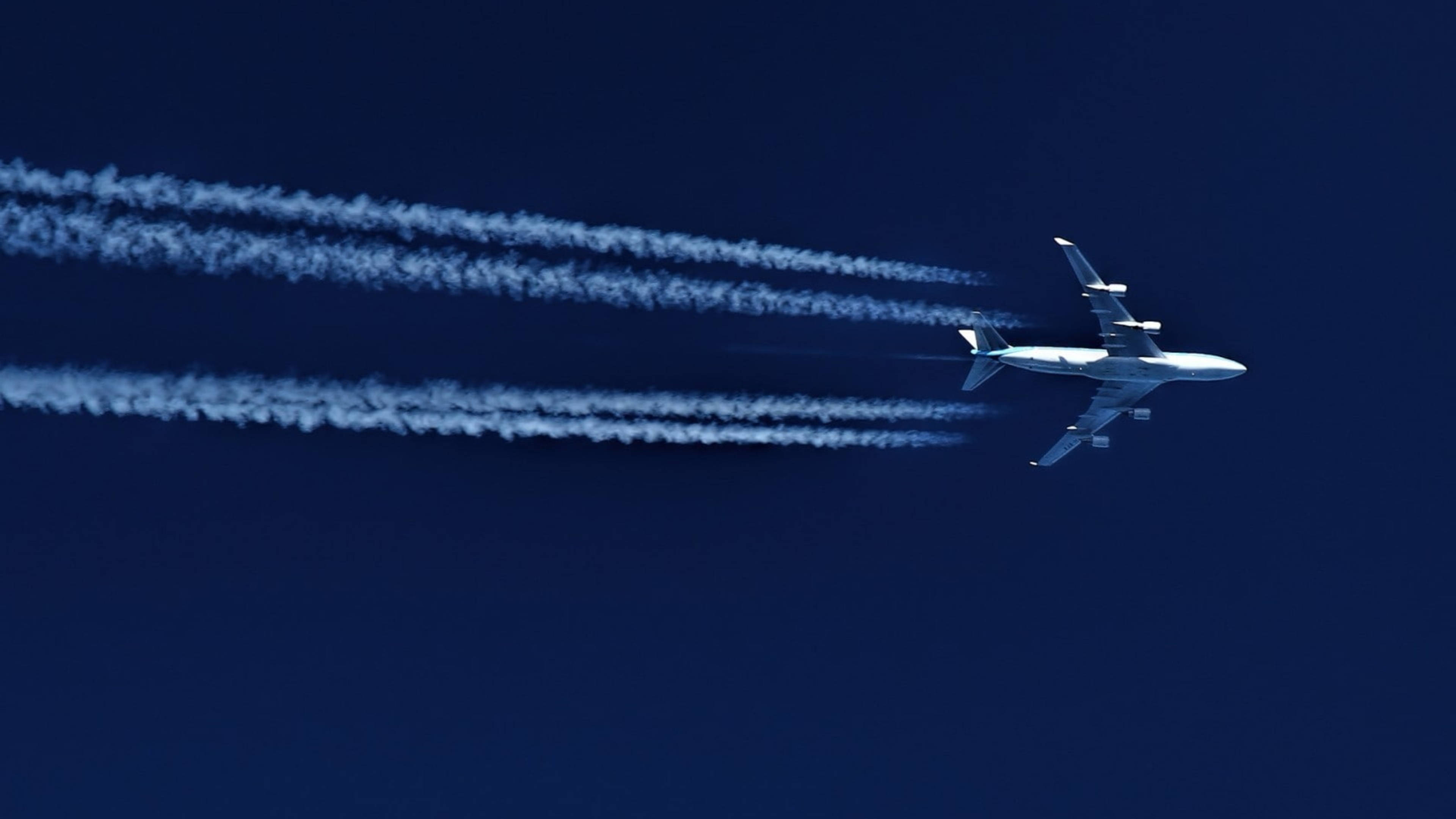 Plane 桌布 壁紙 — 一架白色客機在深藍色的天空中翱翔，留下長長的、縷縷的凝結尾跡。