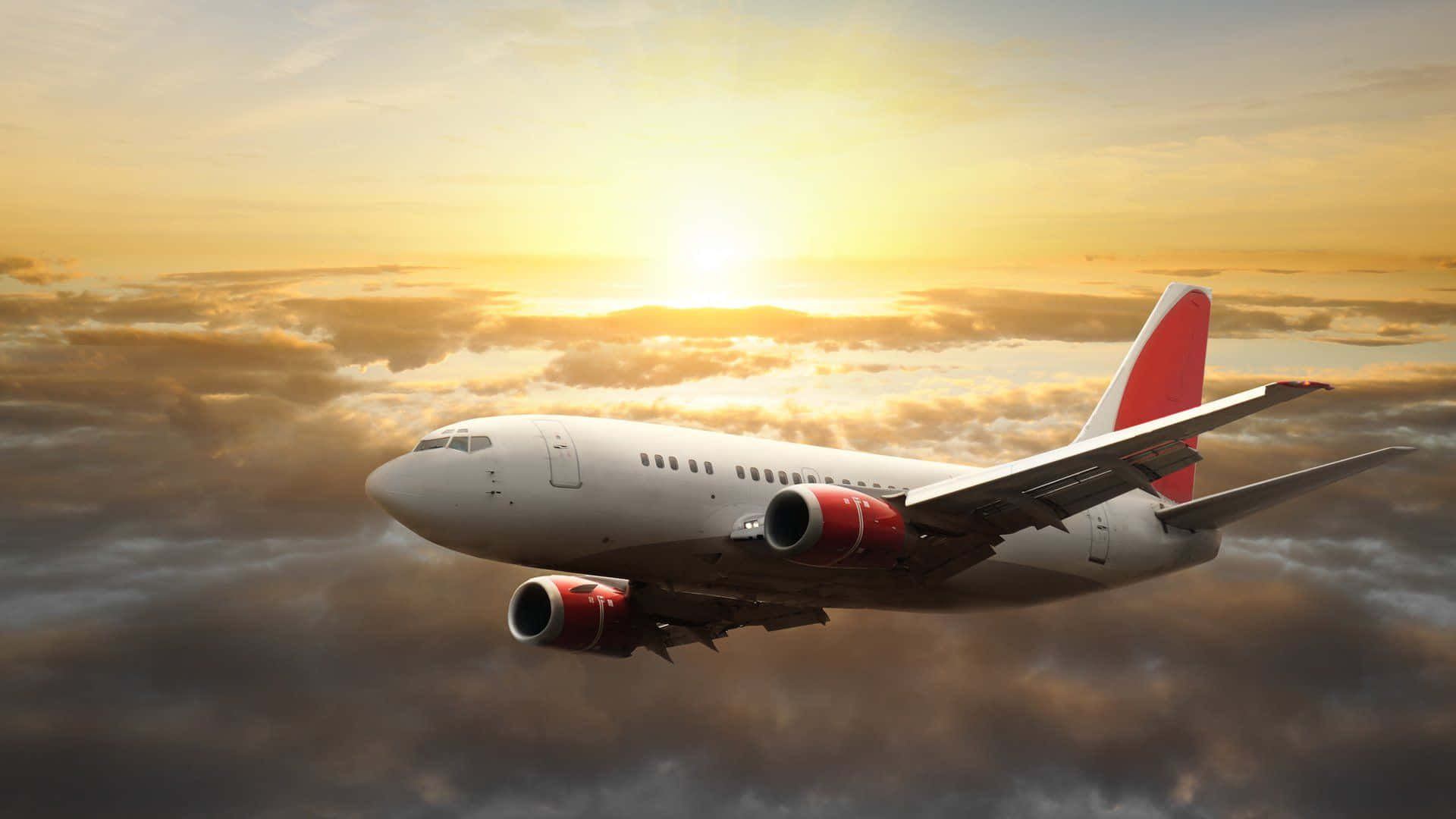Aviation 桌布 壁紙 — 一架白色客機配備紅色引擎和尾翼，在燦爛的日落中翱翔於金色雲層之上。