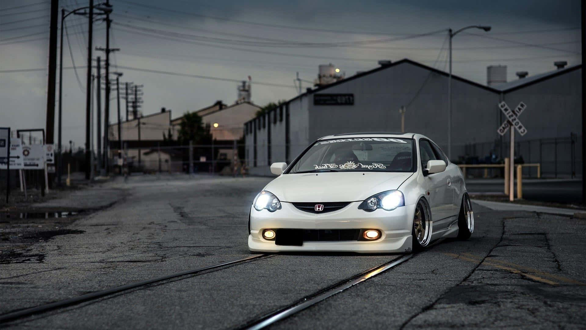 Acura Integra 桌布 壁紙 — 一架白色改裝本田思域在黃昏時低趴於鐵軌上，閃爍的車頭燈照亮了粗糙的工業街道。