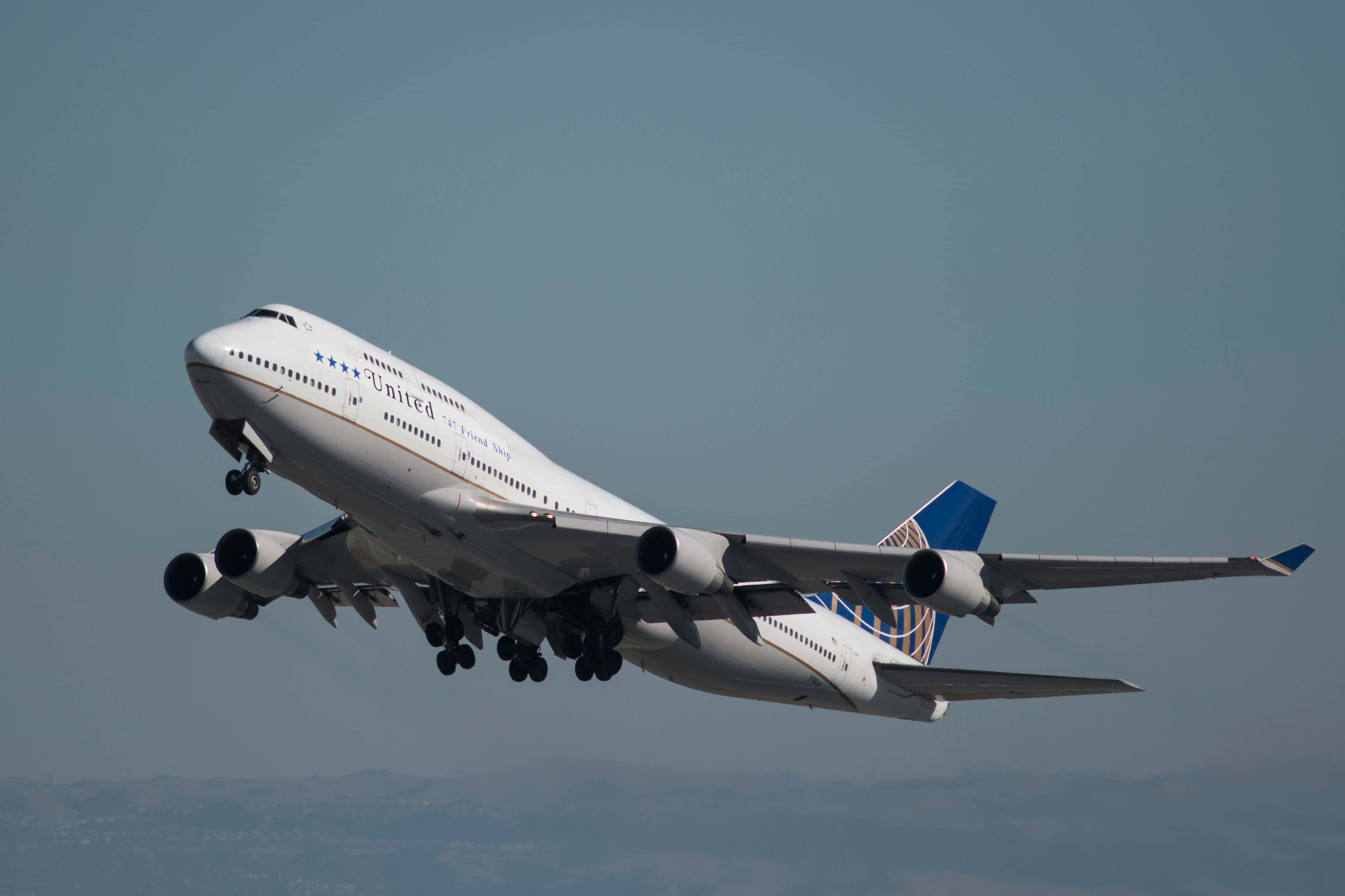 Jumbo Jets 桌布 壁紙 — 一架白色的聯合航空波音747在朦朧的藍天中攀升，下方是遠處的山丘。