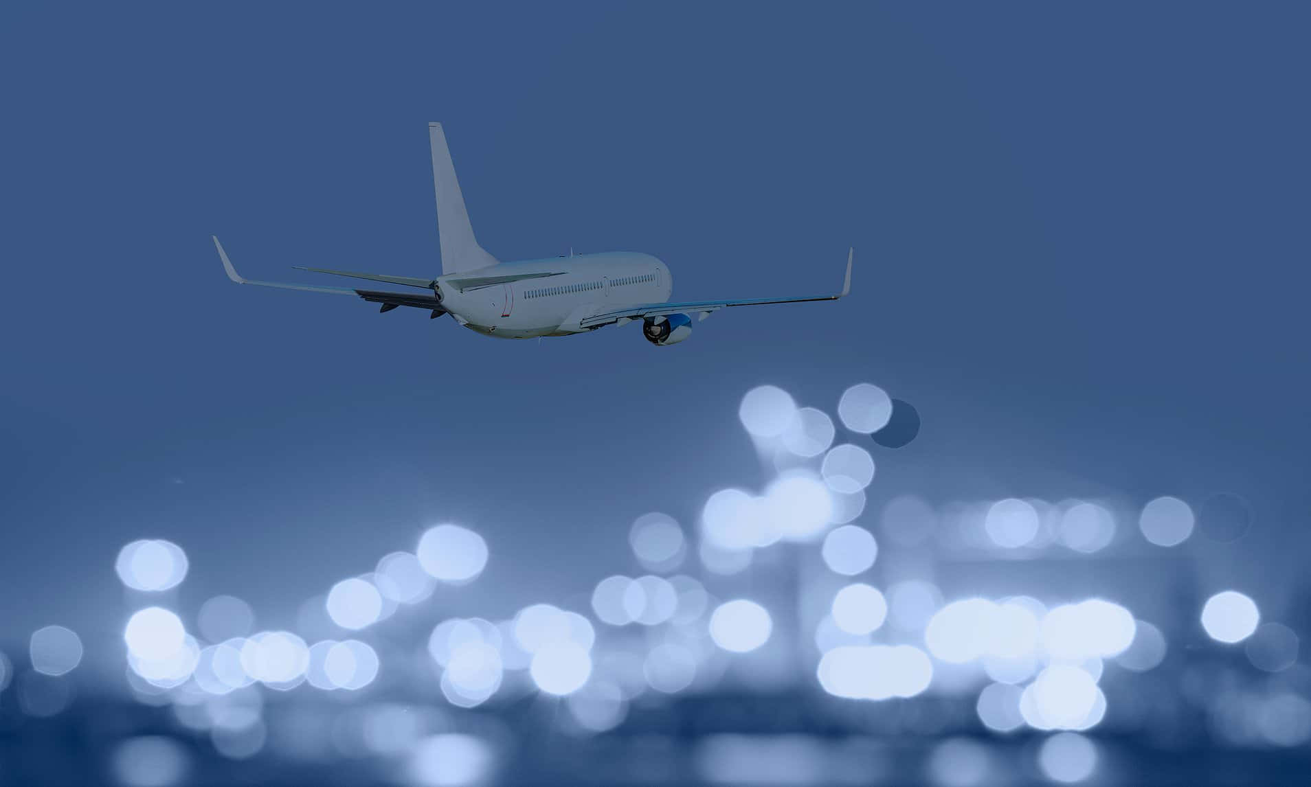 Aviation 桌布 壁紙 — 一架白色飛機在散景燈光照射的機場客運大樓上空，於暮色天空中攀升。