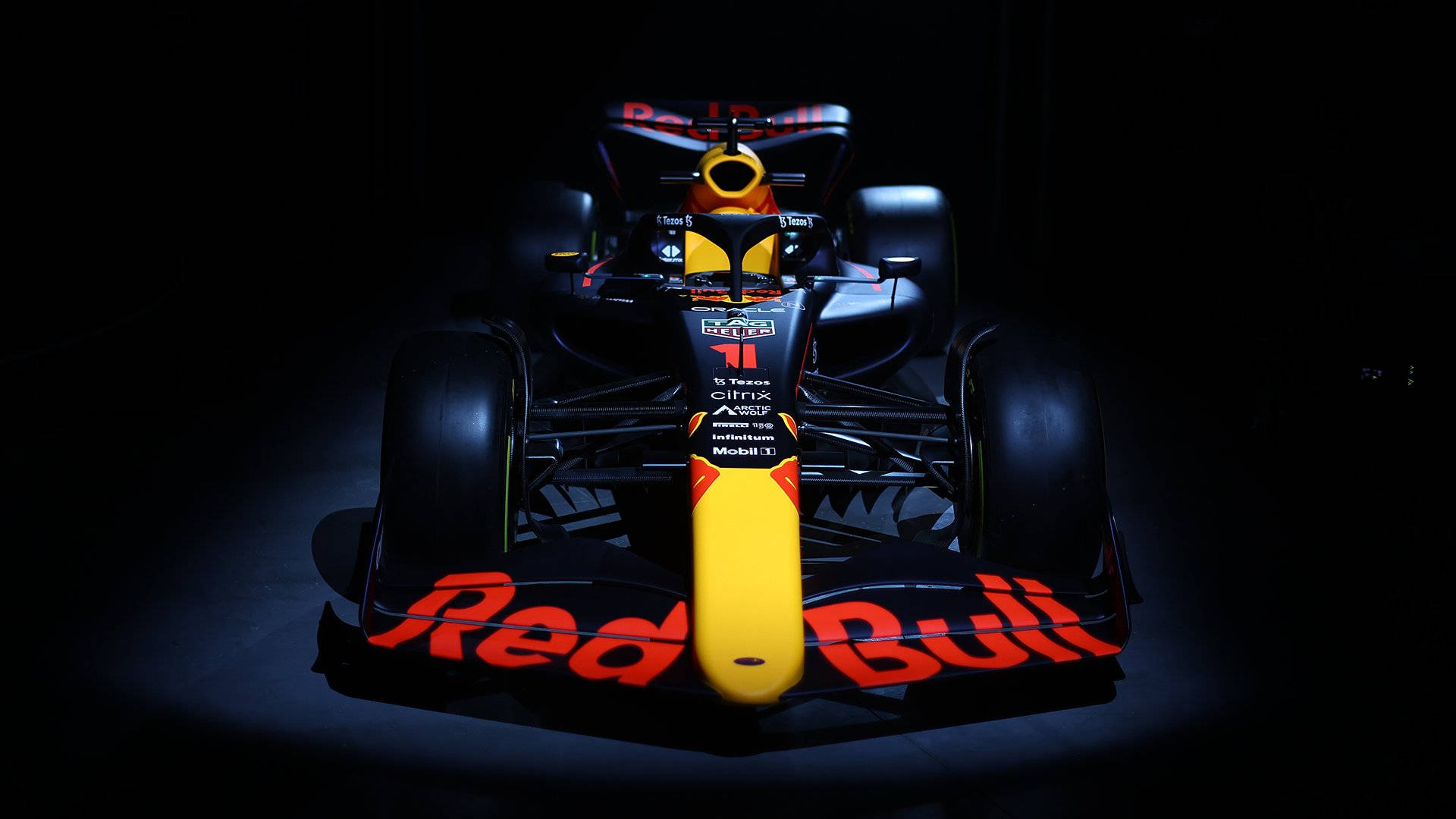 F1 桌布 壁紙 — 一架紅牛一級方程式賽車在黑色背景下被聚光燈照亮，展示其空氣動力學設計和贊助商標誌。