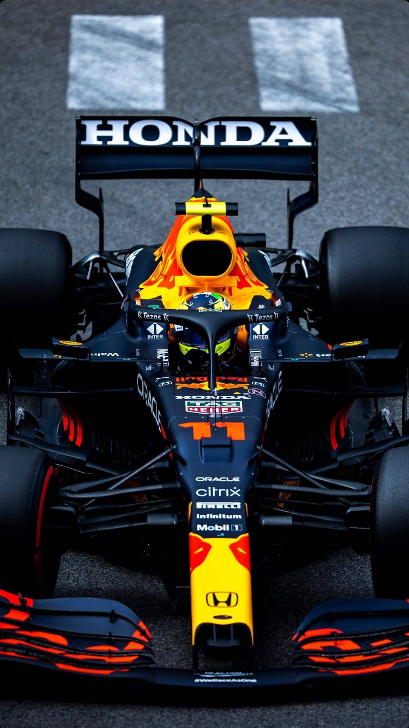 sergio perez 桌布 壁紙 — 一架紅牛車隊一級方程式賽車，帶有鮮豔的橙色和黑色塗裝，停在賽道發車格上，準備高速競賽。