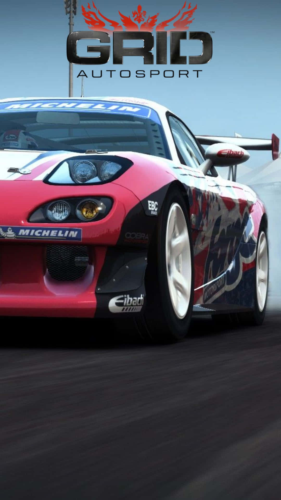 Grid Autosport 桌布 壁紙 — 一架紅色和藍色的賽車在晴朗的天空下，以動態模糊效果和可見的贊助商標誌在賽道上飛馳。