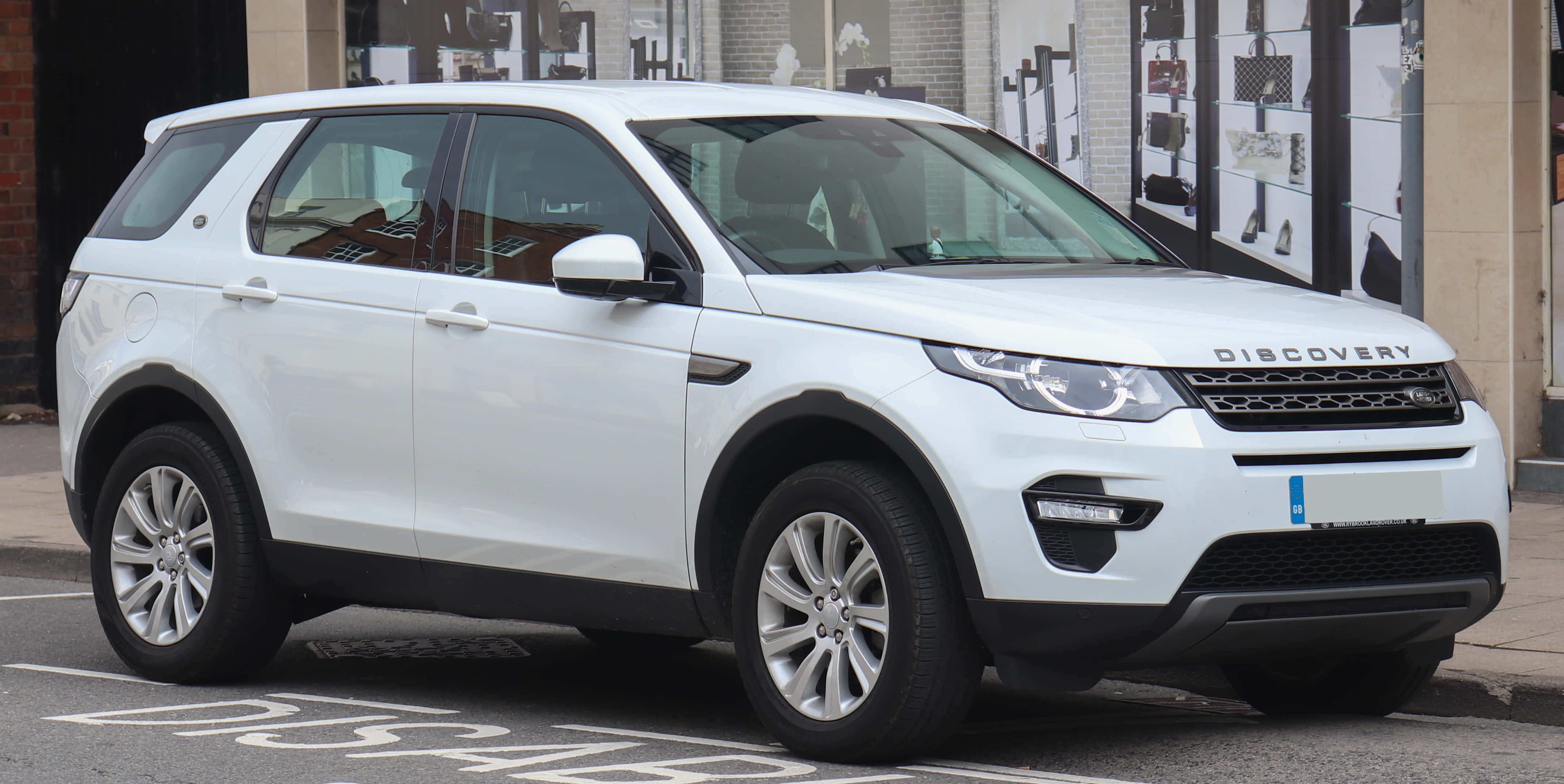 Land Rover Discovery 桌布 壁紙 — 一架純白色 Land Rover Discovery SUV 停泊在城巿街道上，背景有商店門面。