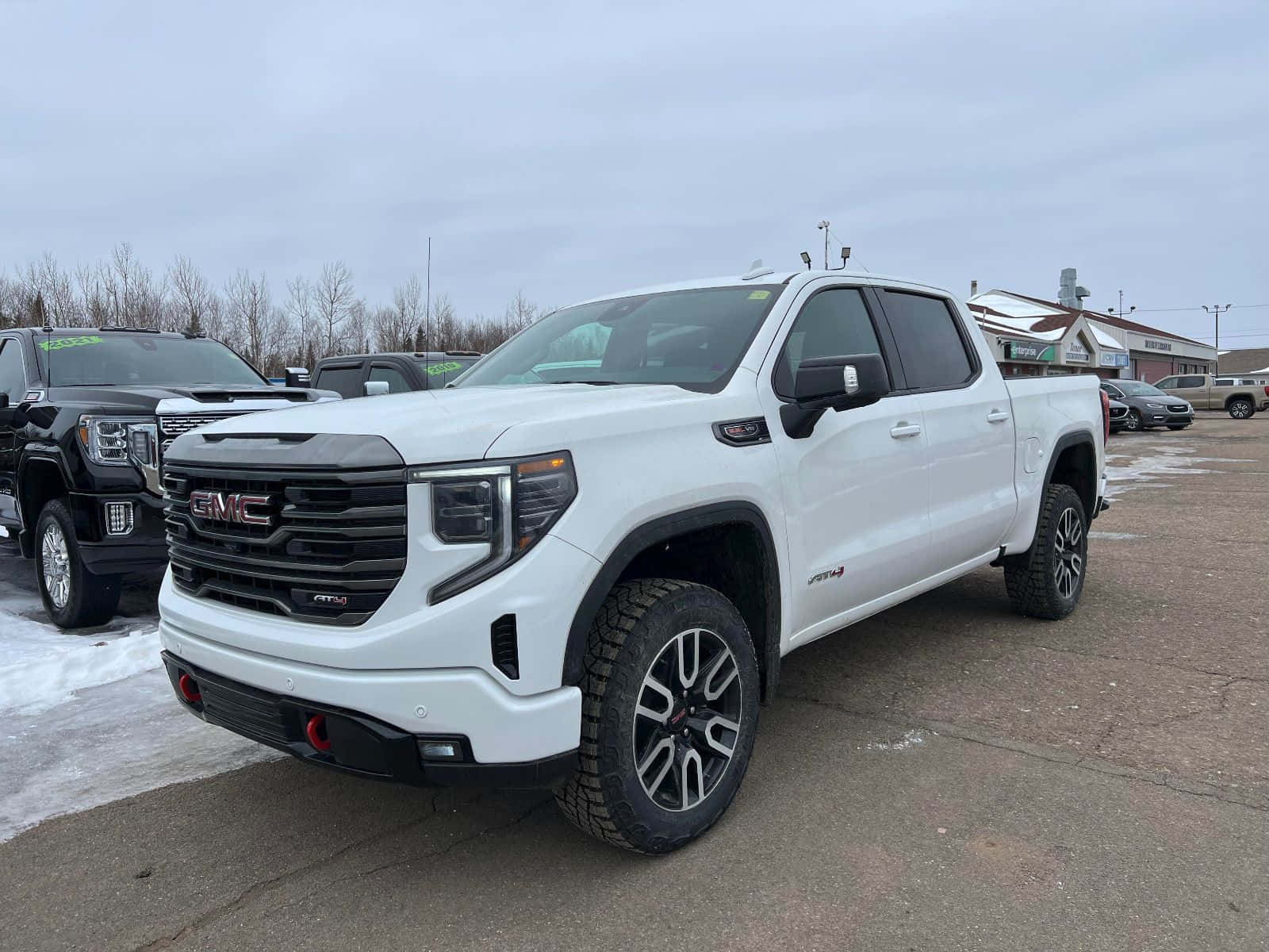 Gmc Sierra 桌布 壁紙 — 一架純白色GMC Sierra AT4 pickup貨車停泊在雪地停車場，周圍有光禿禿的樹木和陰天。