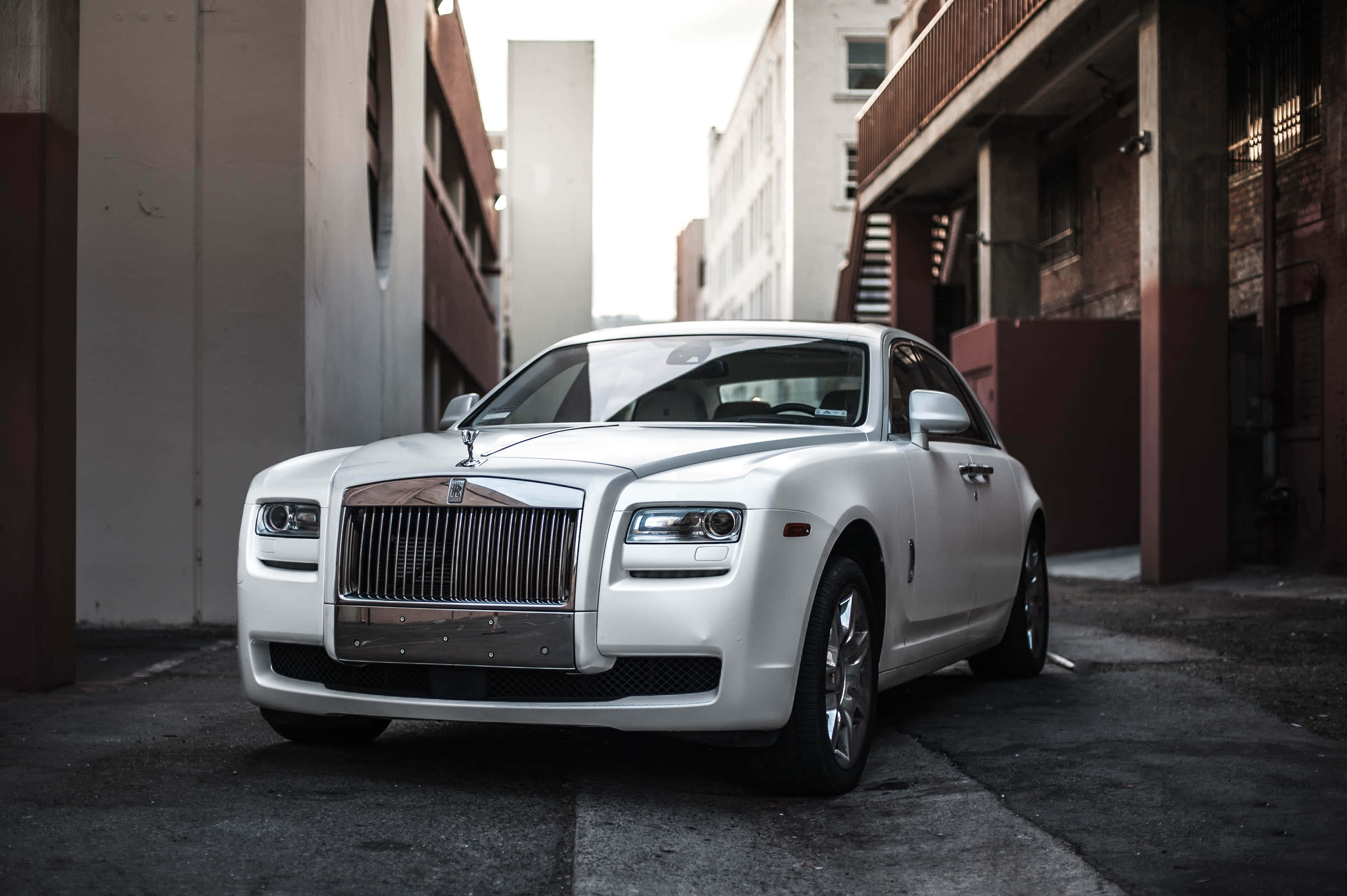 Rolls Royce 桌布 壁紙 — 一架純白色勞斯萊斯 Ghost 停泊在狹窄的城市小巷中，兩旁是風化的建築物。