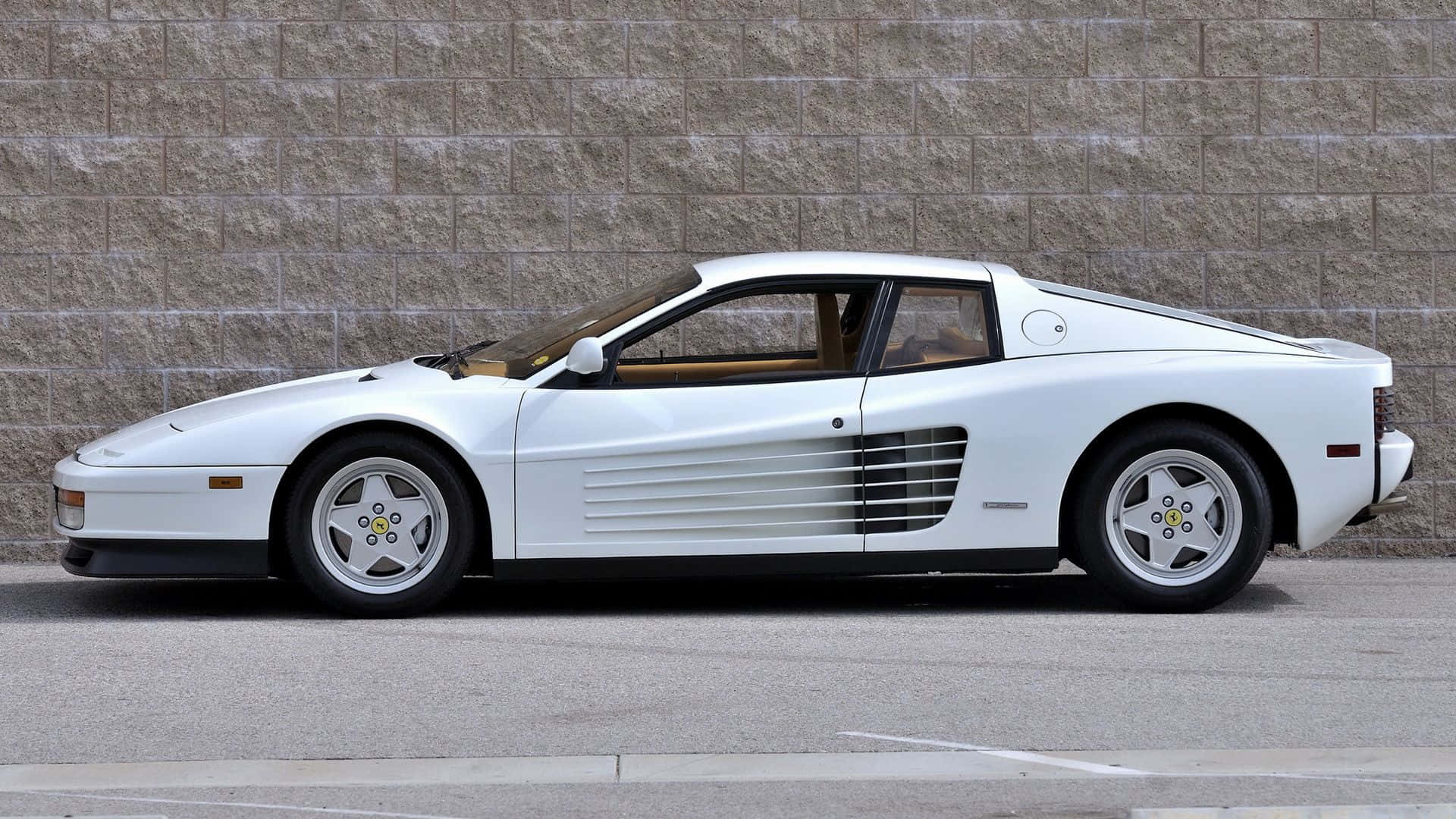 Ferrari Testarossa 桌布 壁紙 — 一架純白色的法拉利 Testarossa 停泊在鋪砌街道上、質感石牆旁邊。