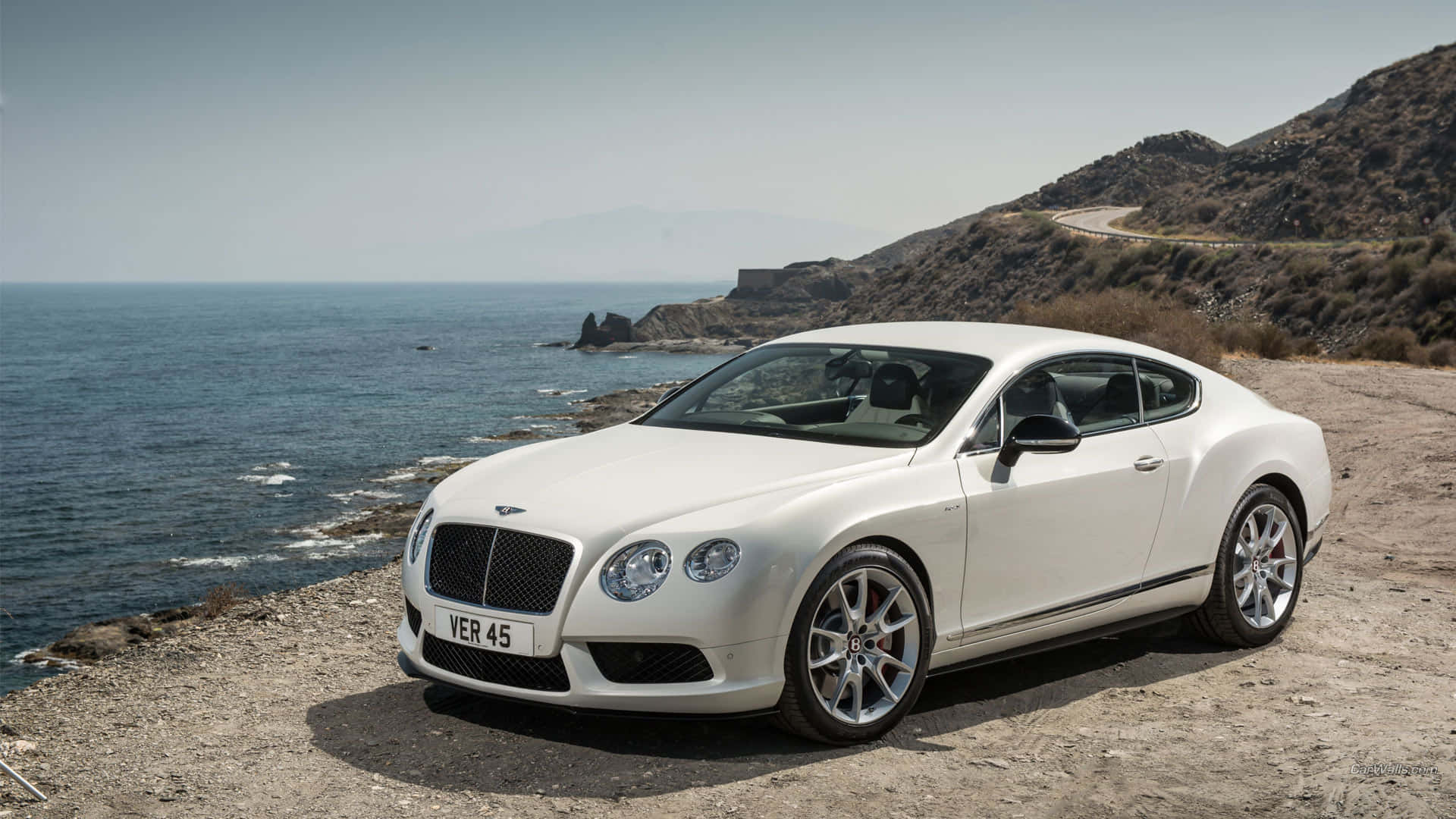 Bentley Continental Gt 桌布 壁紙 — 一架純白色的賓利 Continental GT 停泊在崎嶇的海岸懸崖上，俯瞰深藍色的大海。