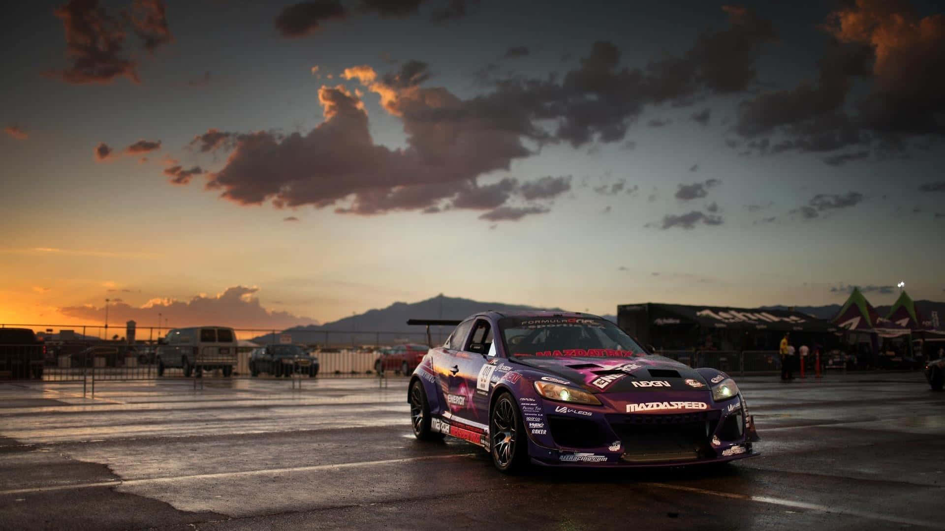 Mazda Rx-8 桌布 壁紙 — 一架紫色Mazda飄移車喺濕滑賽道上，喺橙粉紅雲彩嘅戲劇性日落天空下閃耀。