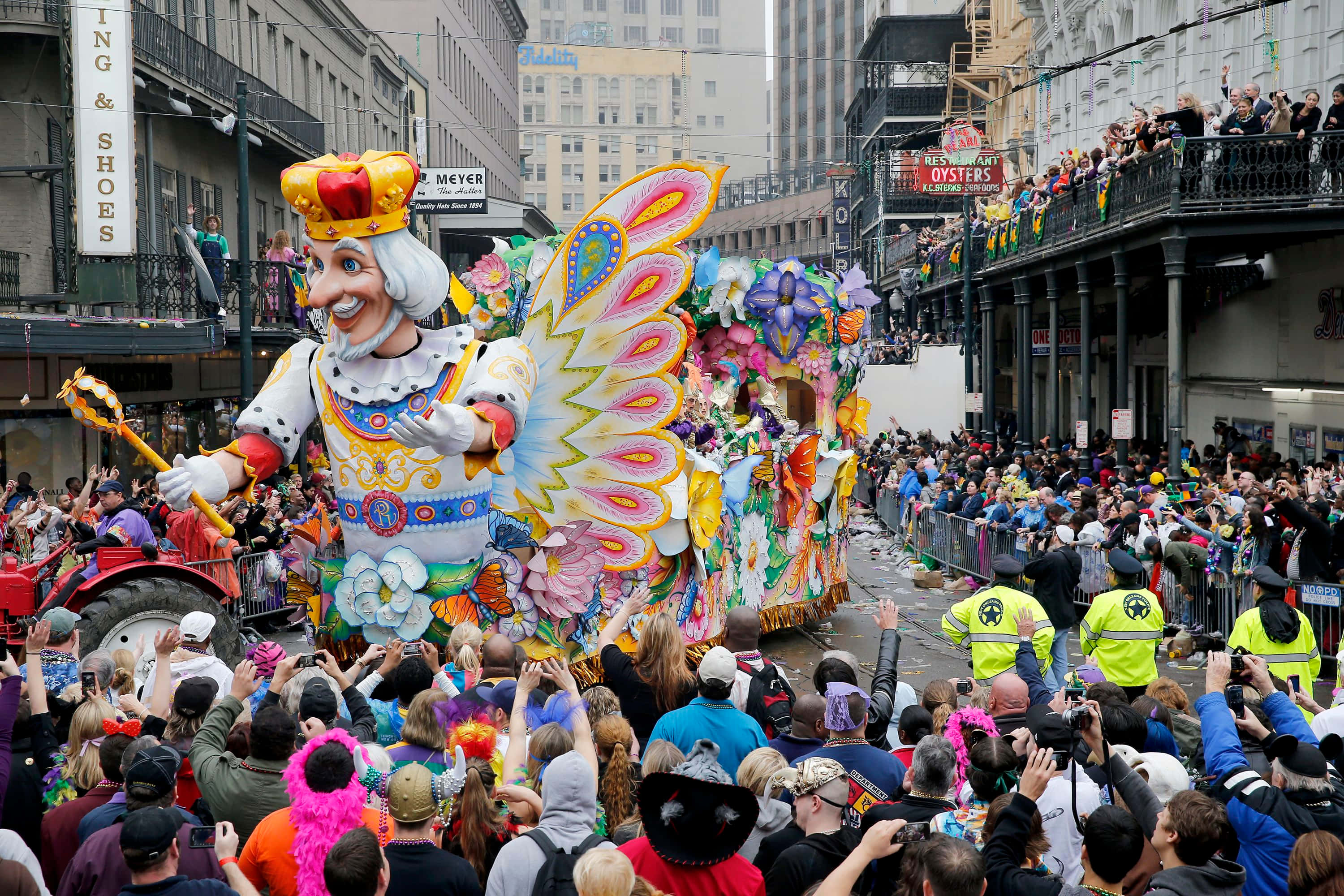 Mardi Gras 桌布 壁紙 — 一架色彩繽紛的狂歡節花車，上面有一個巨大微笑的國王，長著彩色翅膀，穿過新奧爾良擁擠的街道。