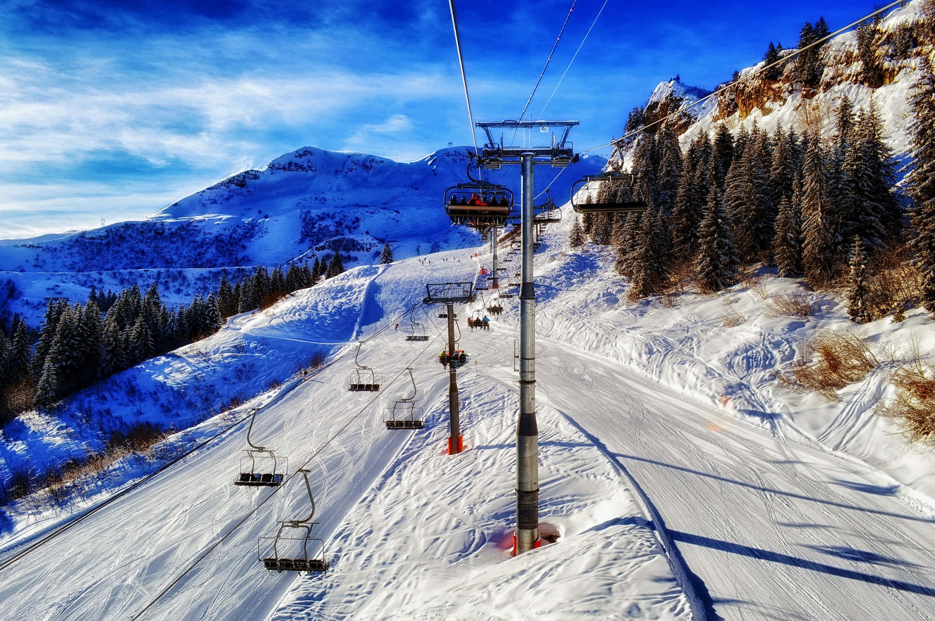 Ski Resort 桌布 壁紙 — 一架色彩鮮豔的滑雪纜車在藍天白雲下，沿著白雪覆蓋的山坡上升。