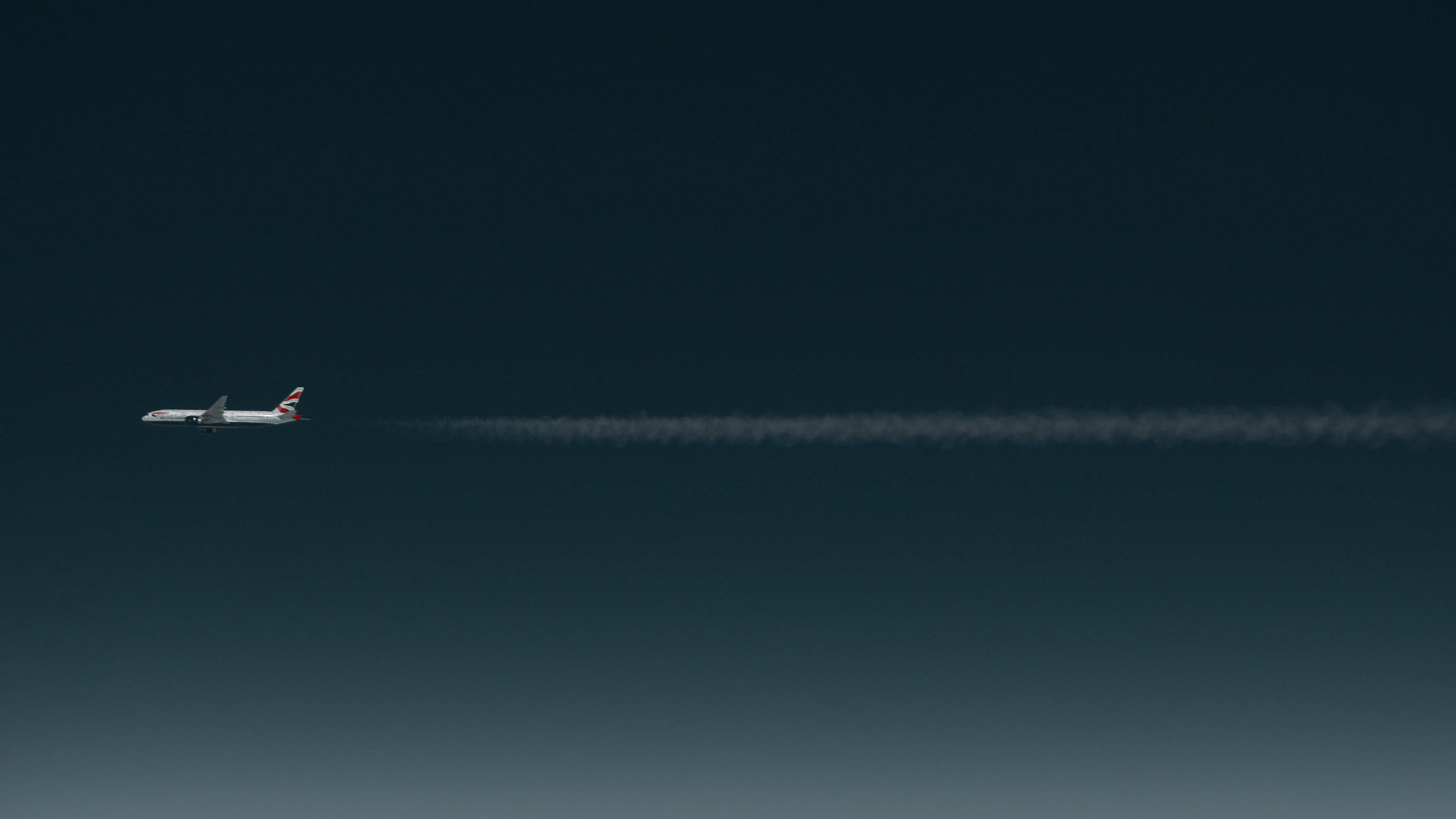 飛機 桌布 壁紙 — 一架英國航空公司的飛機獨自飛翔在深藍色漸變的天空中，留下一條長長的白色的凝結尾跡。