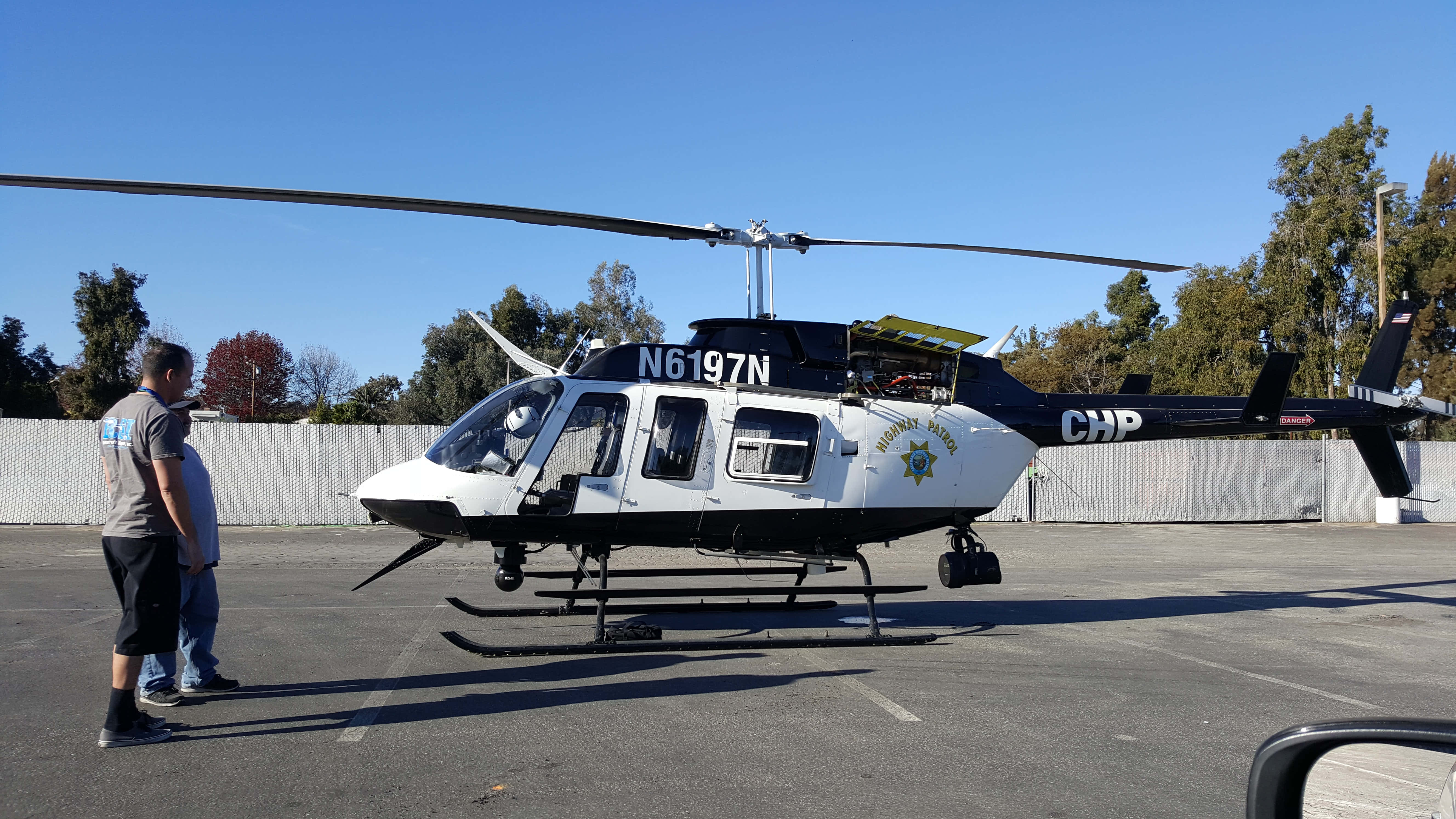 直升機 桌布 壁紙 — 一架註冊編號為N6197N的加州公路巡邏直升機停在瀝青地面上，天空清澈湛藍，兩名男子正在觀察它。