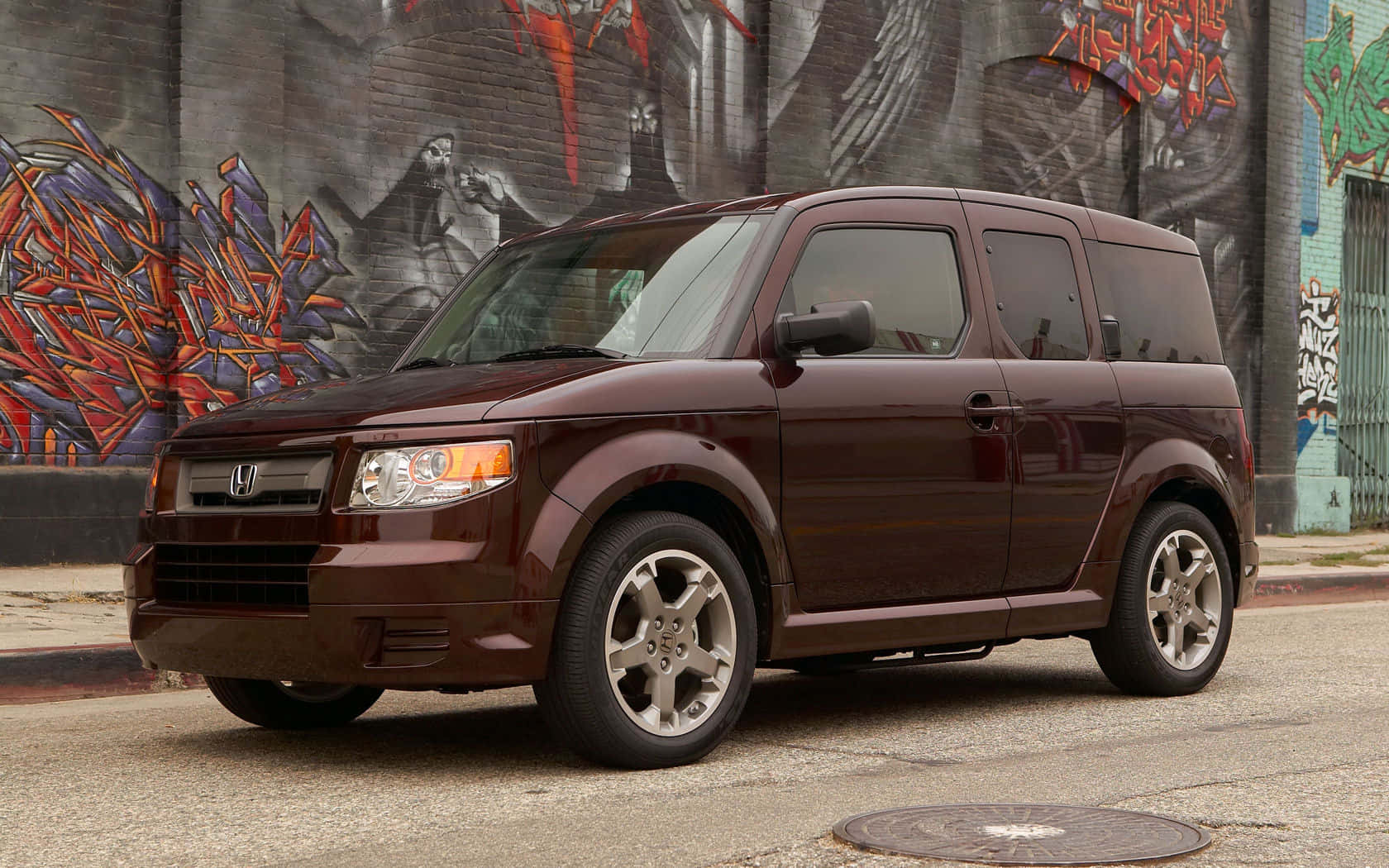 Honda Element 桌布 壁紙 — 一架酒紅色本田 Element 停泊在一條佈滿砂礫的街道上，旁邊是一幅充滿活力的塗鴉磚牆。