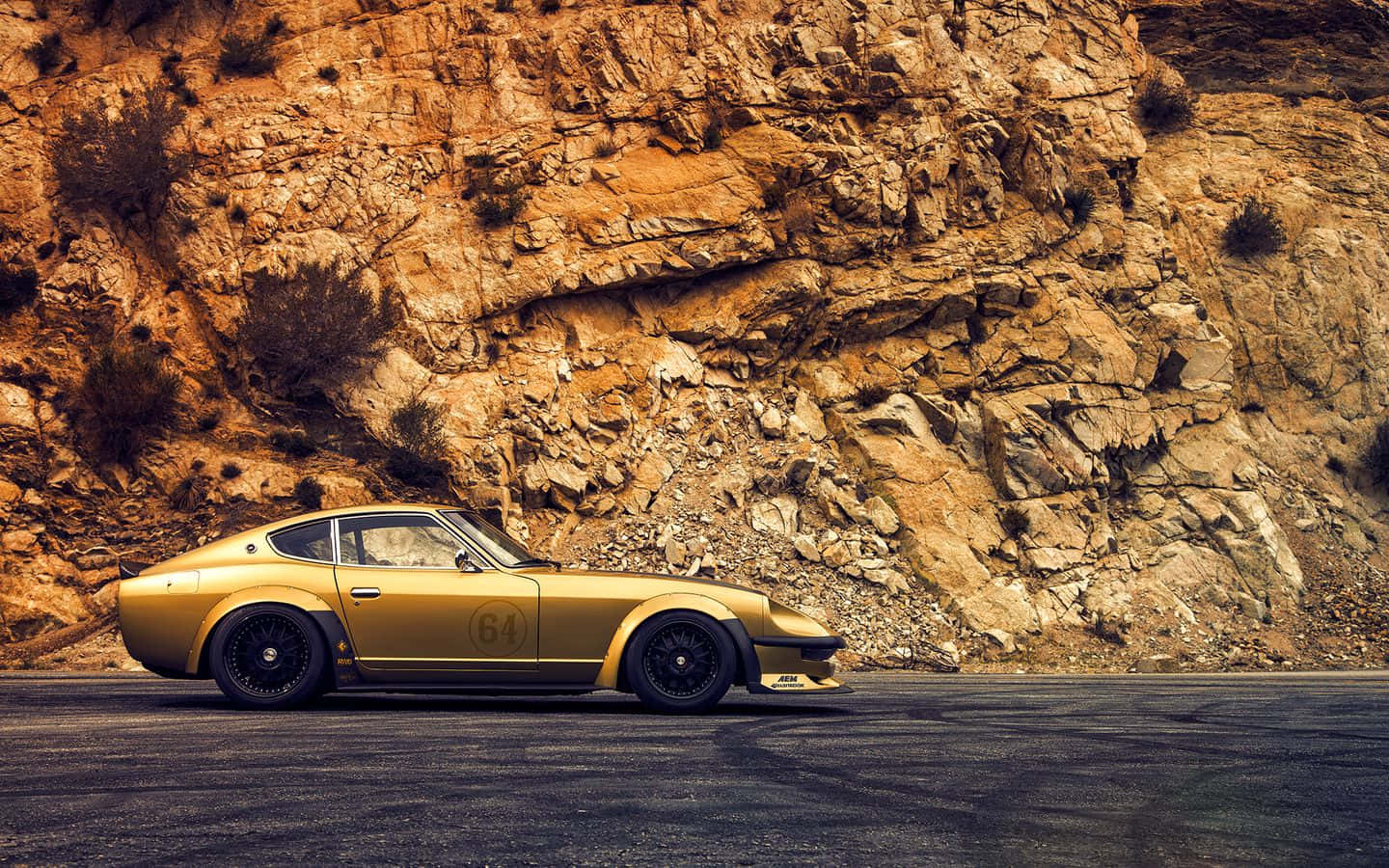 Datsun 桌布 壁紙 — 一架金色復古賽車，編號64，停泊在蜿蜒的道路上，背景是崎嶇的岩石懸崖。