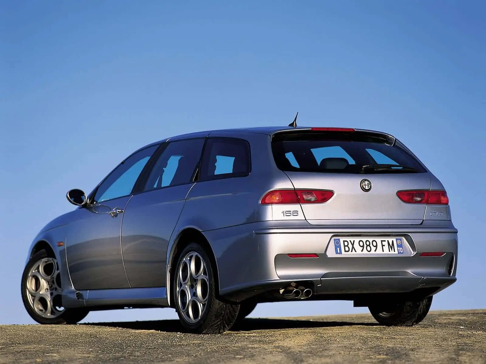 Alfa Romeo 156 桌布 壁紙 — 一架銀色 Alfa Romeo 156 旅行車停泊在碎石平原上，天空清澈湛藍。