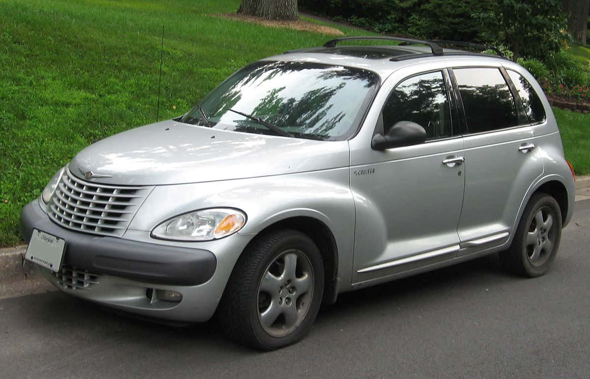 Chrysler Pt Cruiser 桌布 壁紙 — 一架銀色 Chrysler PT Cruiser 在明亮日光下停泊在街道上，旁邊是翠綠茂盛的草坪。