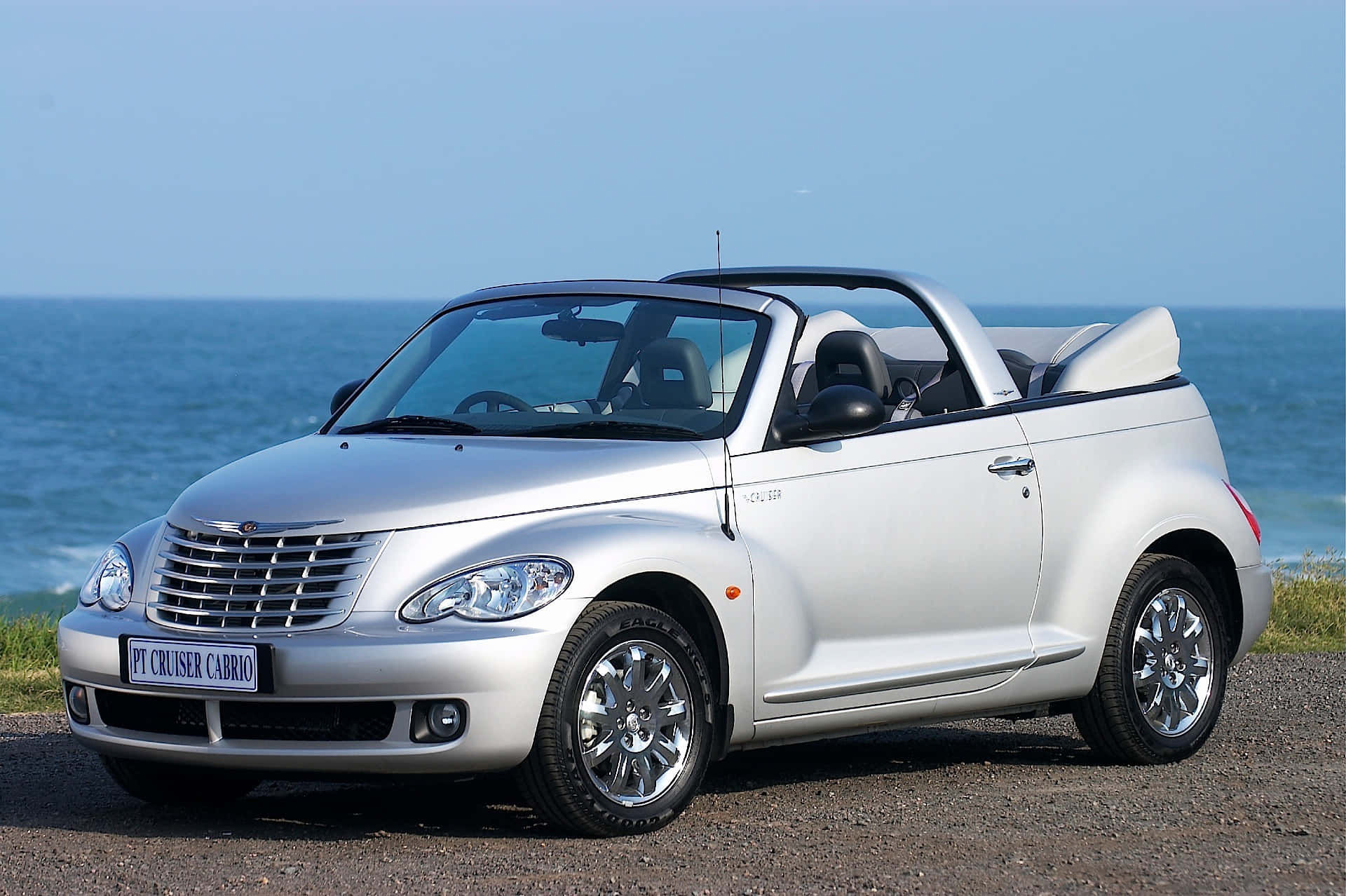 Chrysler Pt Cruiser 桌布 壁紙 — 一架銀色 Chrysler PT Cruiser Cabrio 開篷車停泊在碎石海灘上，背景係海洋同晴朗嘅天空。