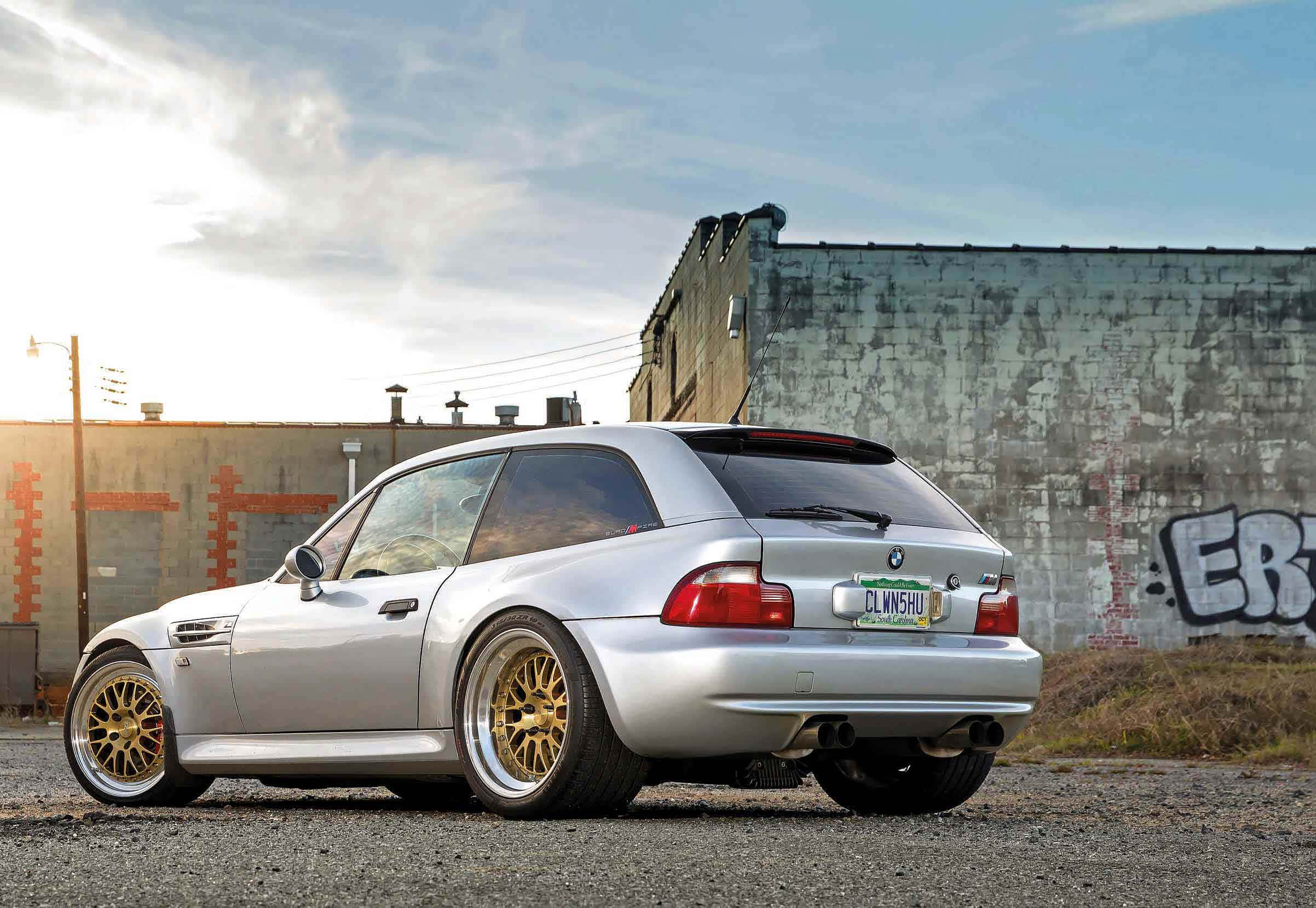 Bmw Z3 桌布 壁紙 — 一架銀色BMW M3配金色輪圈，在日落時停泊在碎石上，旁邊是佈滿塗鴉的工業牆。