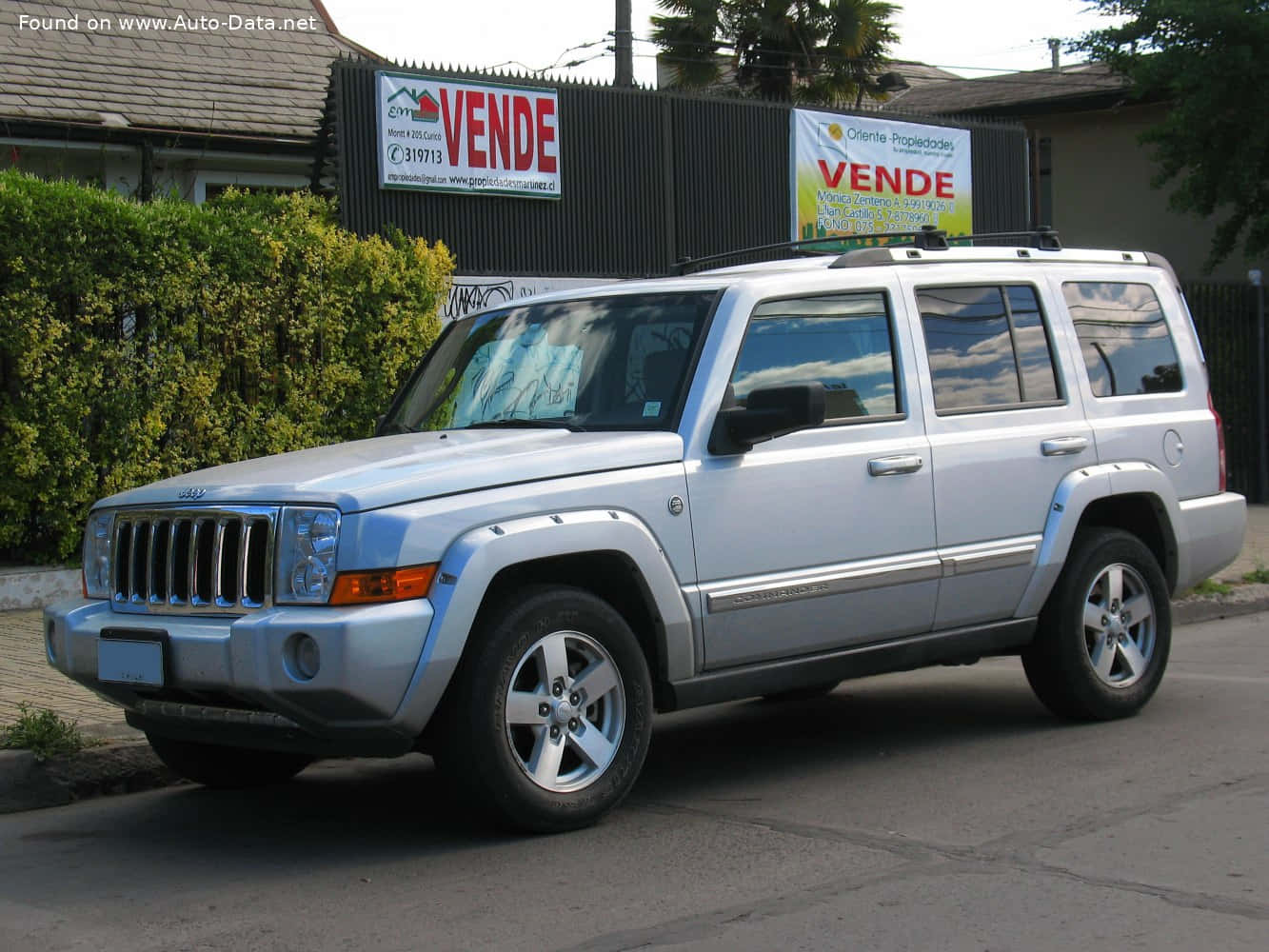 Jeep Commander 桌布 壁紙 — 一架銀色Jeep Cherokee SUV停泊在街上，旁邊有綠色灌木叢和帶有「Vende」標誌的圍欄。