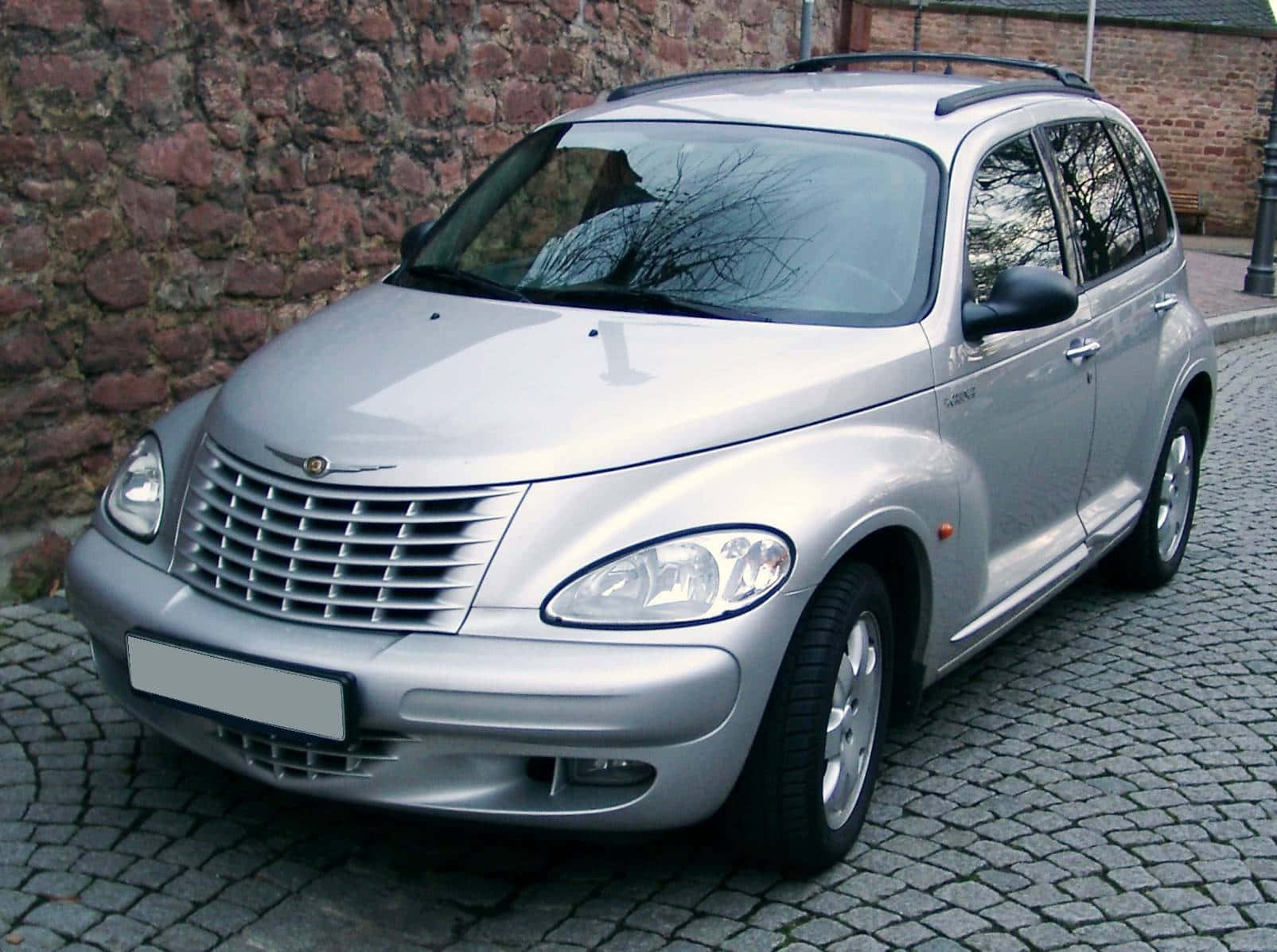 Chrysler Pt Cruiser 桌布 壁紙 — 一架銀色克萊斯勒PT Cruiser停泊在紅磚牆旁邊的鵝卵石街道上。