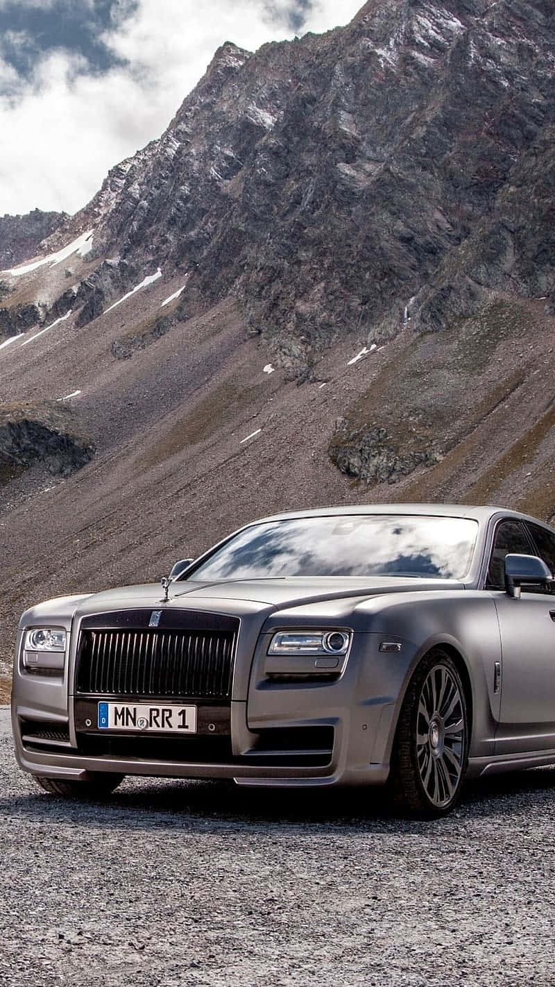 Rolls Royce 桌布 壁紙 — 一架銀色勞斯萊斯停泊在碎石路上，背後是白雪覆蓋的高聳山脈，天空多雲。