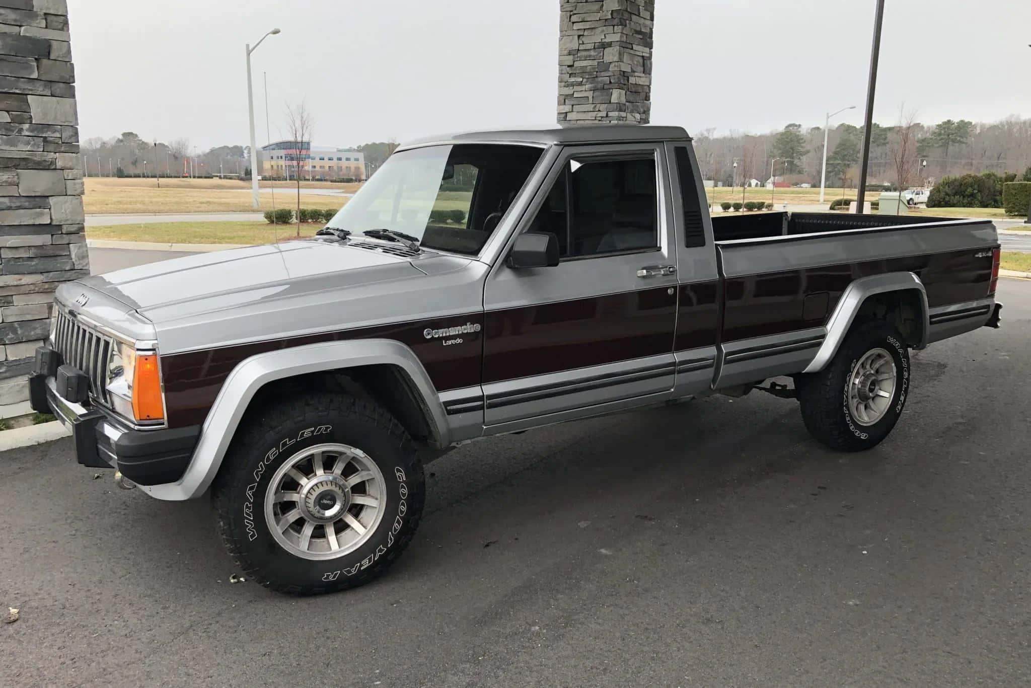 Jeep Comanche 桌布 壁紙 — 一架銀色和栗色的Jeep Comanche pickup貨車停泊在瀝青路上，旁邊是石柱，天空多雲。