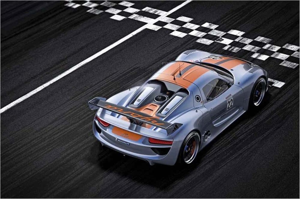 Car Racing 桌布 壁紙 — 一架銀色和橙色的保時捷賽車從高角度俯瞰，在黑暗的賽道上越過格仔旗終點線。