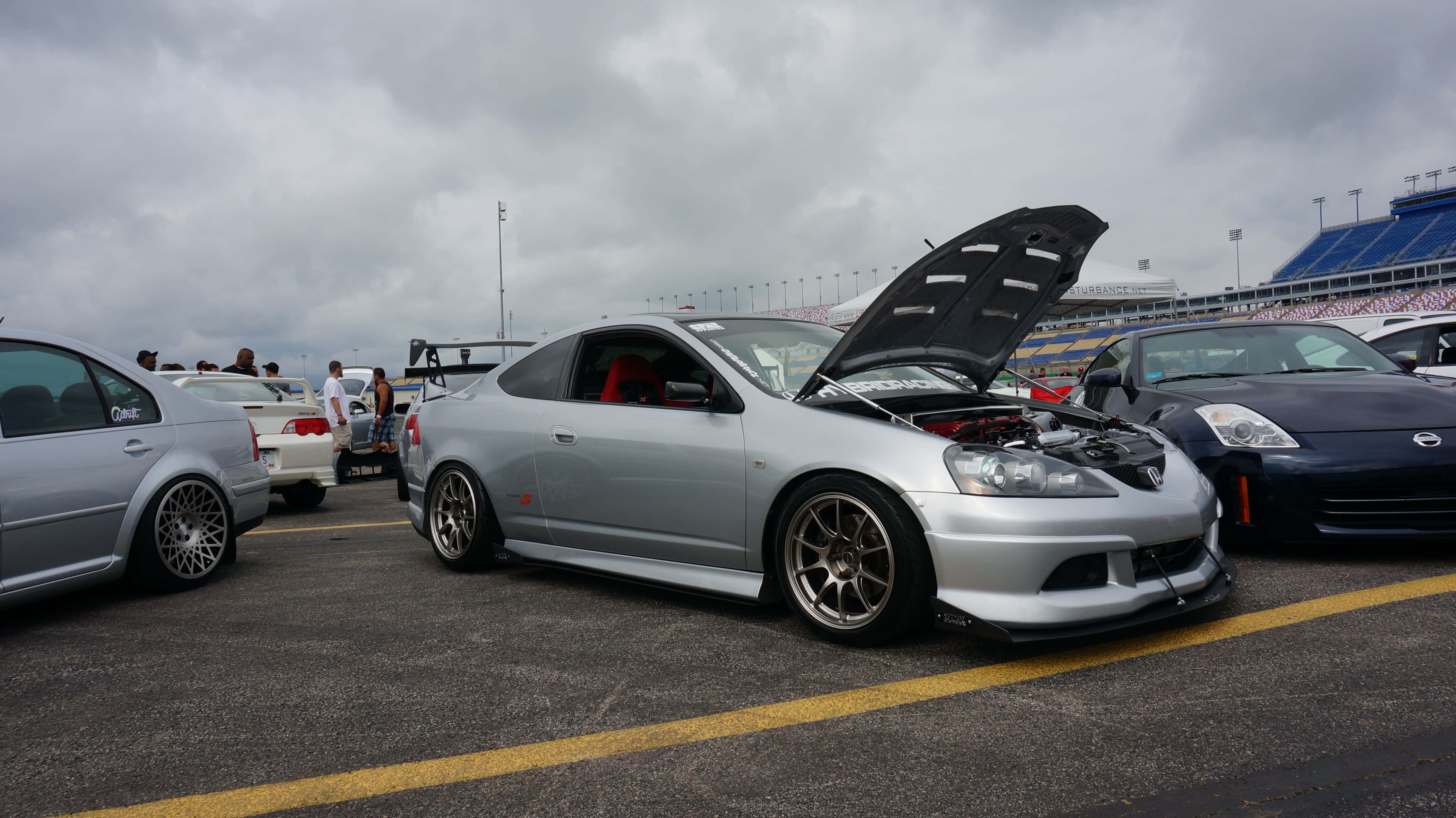Rsx Type-s 桌布 壁紙 — 一架銀色改裝跑車打開引擎蓋，在陰天下的賽車場停車場展示定製引擎。